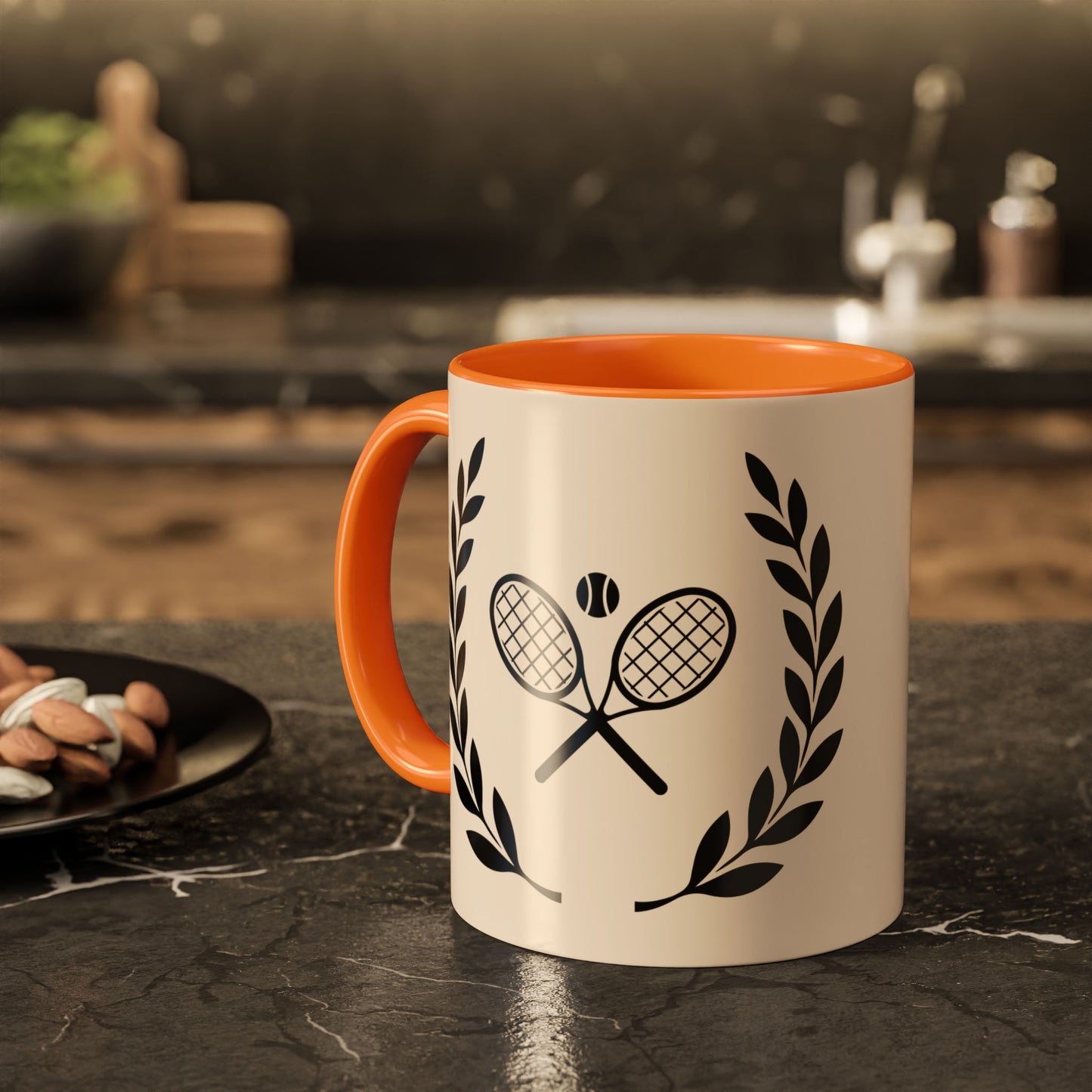 Tennis Coffee Mug A ceramic mug with a cream-colored exterior and bright orange handle/interior, featuring a black graphic of crossed tennis rackets with a tennis ball and laurel wreaths, set on a dark kitchen countertop.