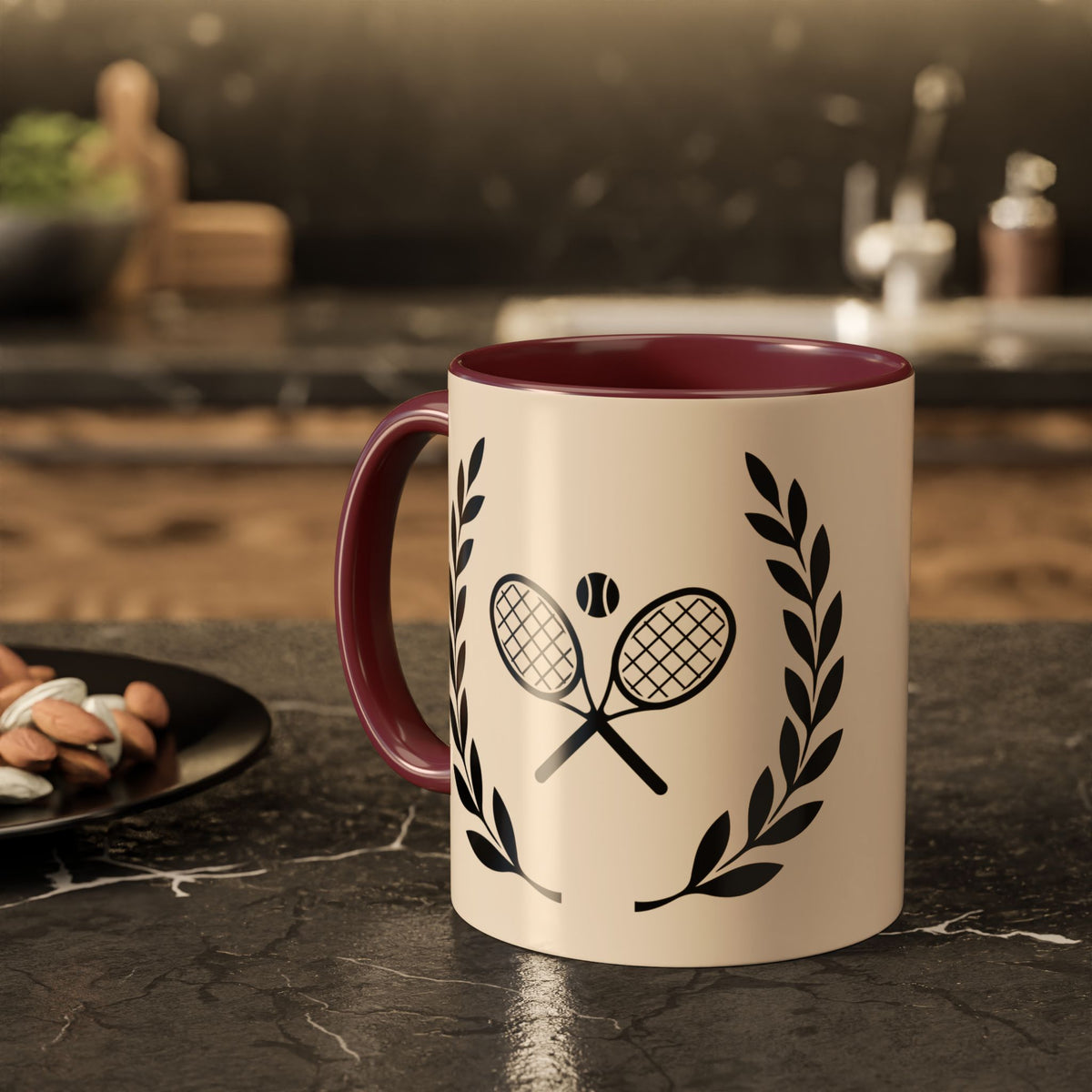 Tennis Coffee Mug A ceramic mug with a cream-colored exterior, dark red interior, and black tennis racket and laurel wreath graphic, set on a dark kitchen countertop.