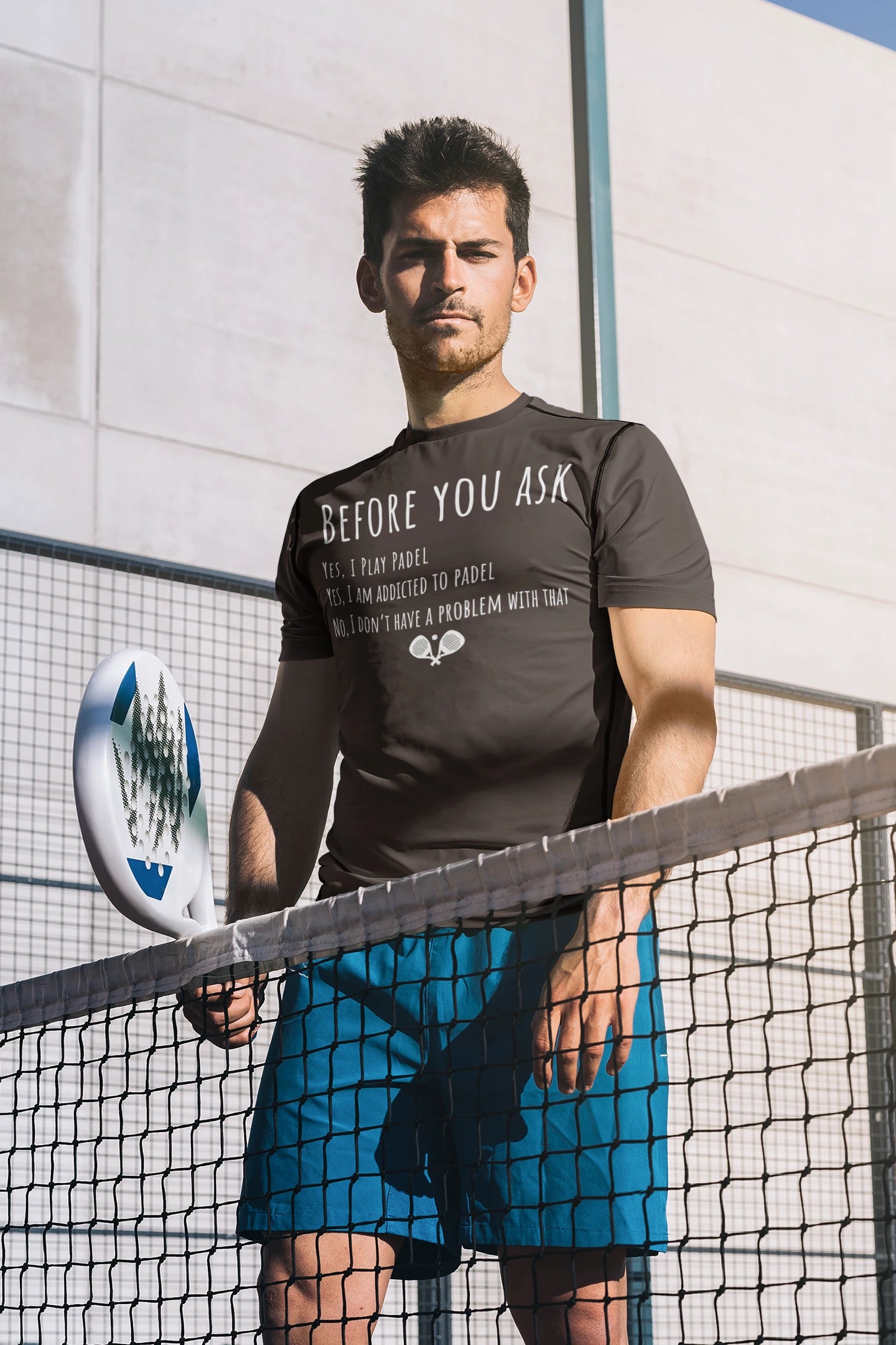 Man holding a padel on a tennis court with a t-shirt and shorts.