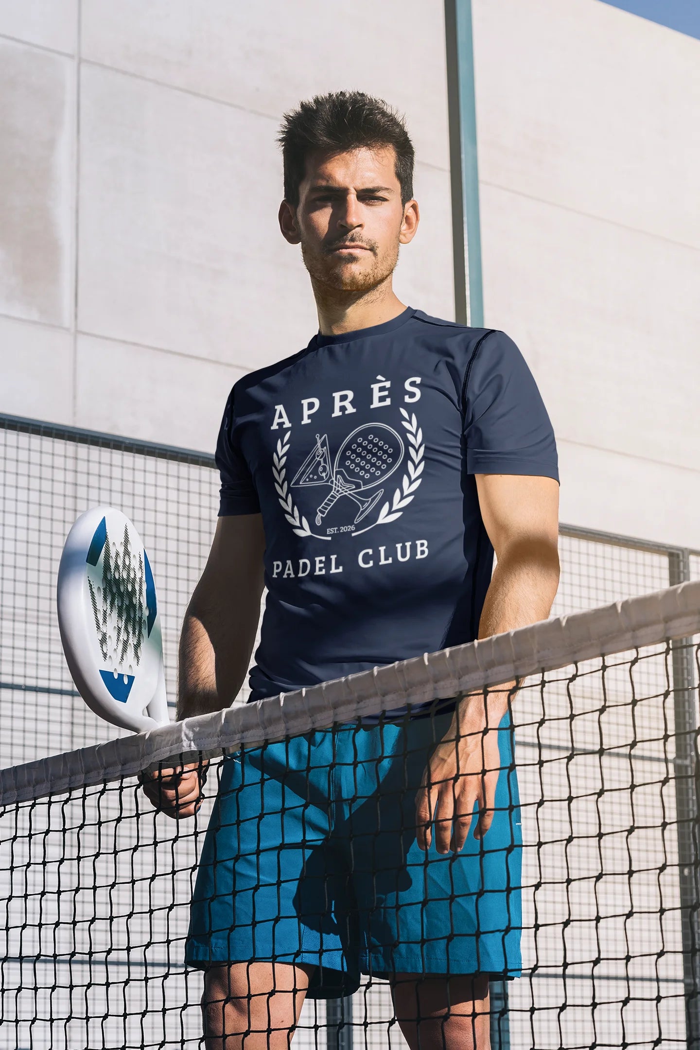 Padel Club Shirt Man holding a paddle on a tennis court wearing an 'Apres Padel Club' t-shirt.
