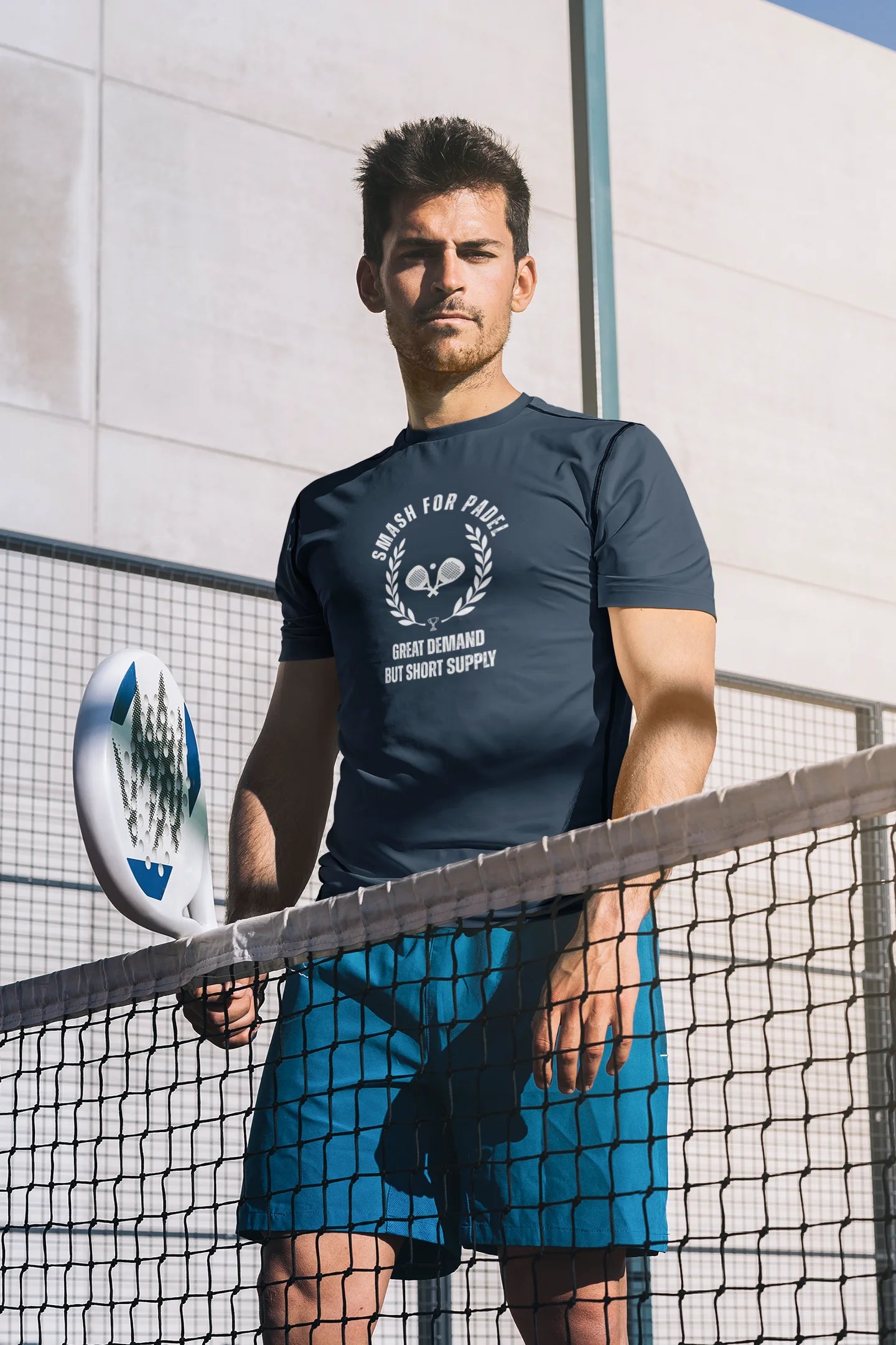 Man holding a paddle on a tennis court with a branded t-shirt