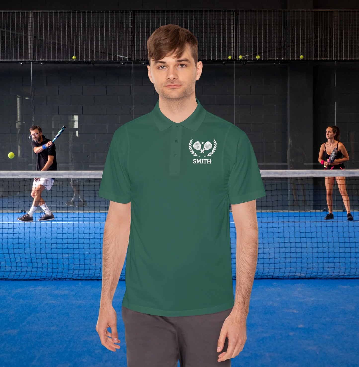 addicted to padel A man wearing a dark green polo shirt with a white 'SMITH' tennis logo on the chest, standing in front of a tennis court with players in the background.