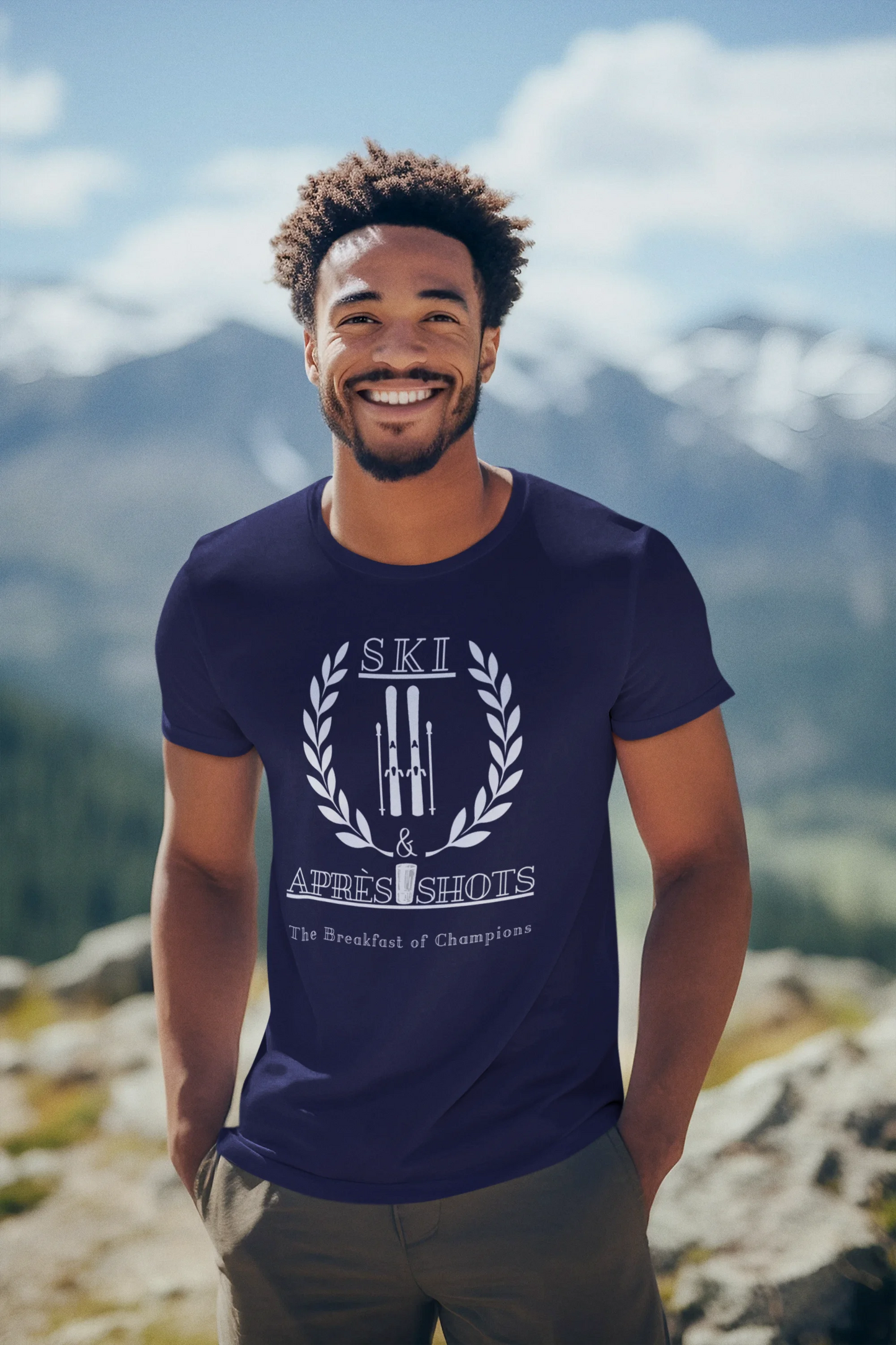 Man wearing a blue t-shirt with a logo and text, standing in a mountainous landscape.