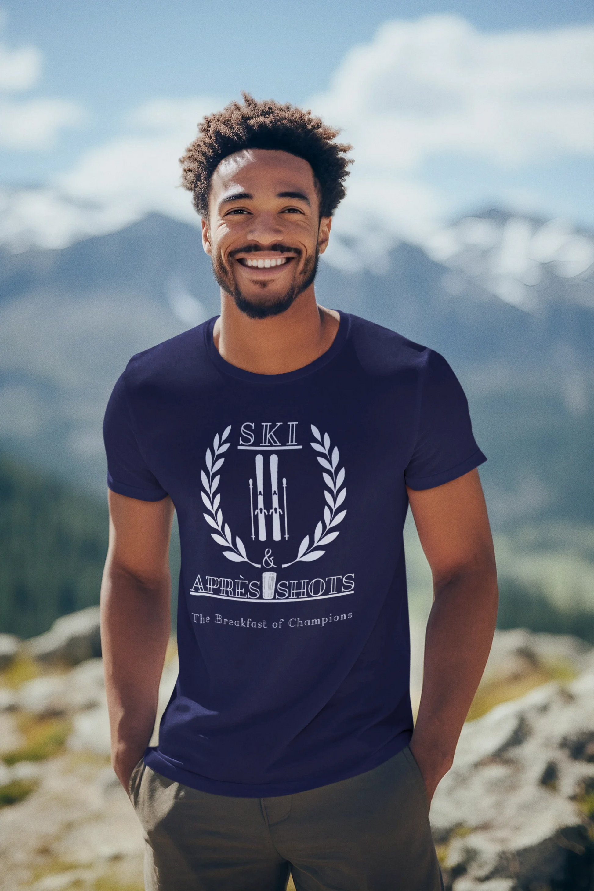 Man wearing a blue t-shirt with a logo and text, standing in a mountainous landscape.
