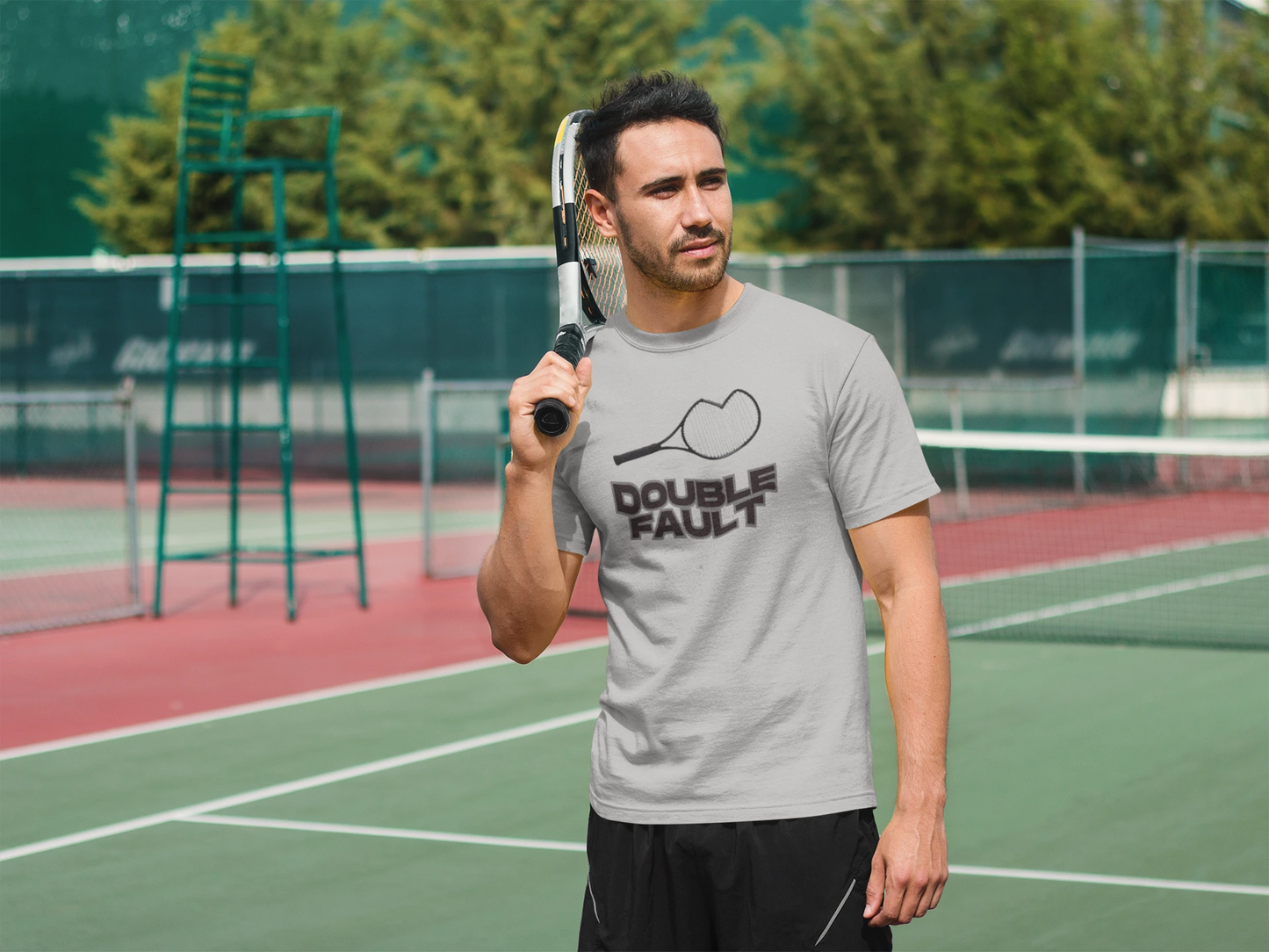 Double Fault Tee Man holding a tennis racket on a tennis court wearing a gray t-shirt with 'Double Fault' text.