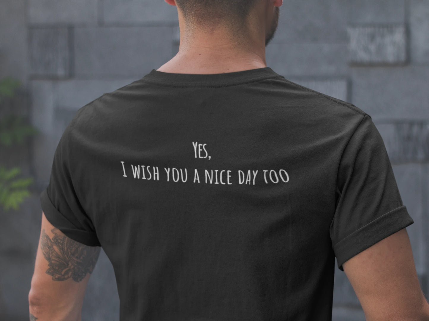 Person wearing a black t-shirt with text on the back, standing against a stone wall.