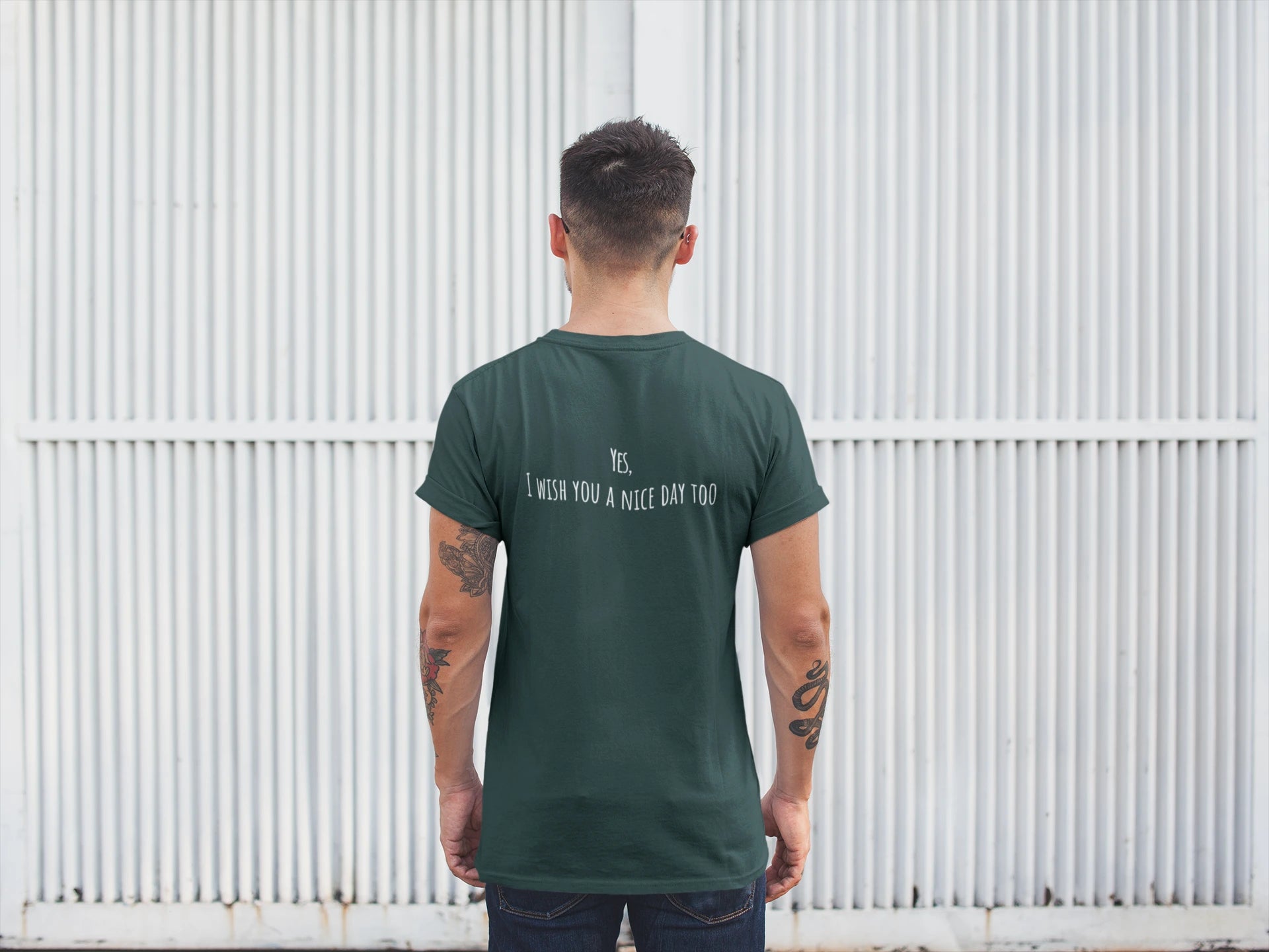 Man wearing a green t-shirt with text on the back, standing against a white corrugated metal wall.