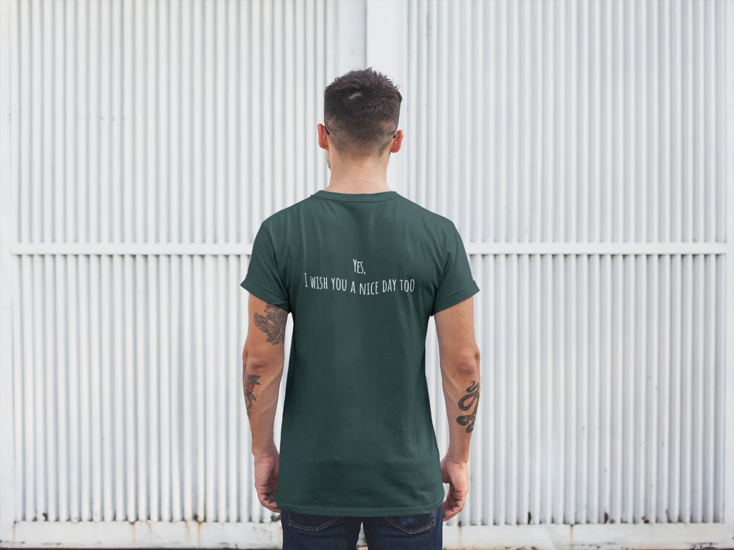 Man wearing a green t-shirt with text on the back, standing against a white corrugated metal wall.