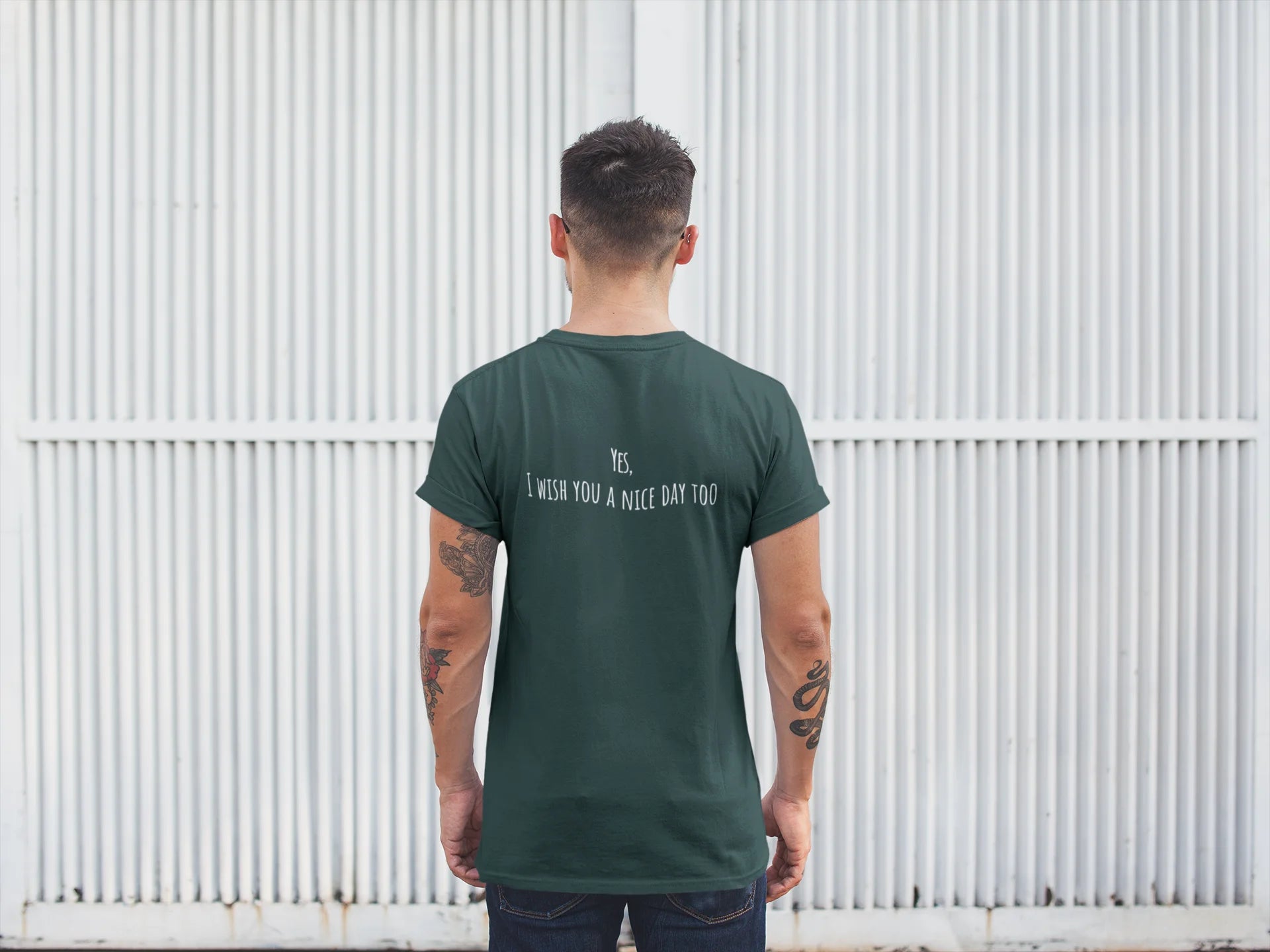 Man wearing a green t-shirt with text on the back, standing against a white corrugated metal wall.