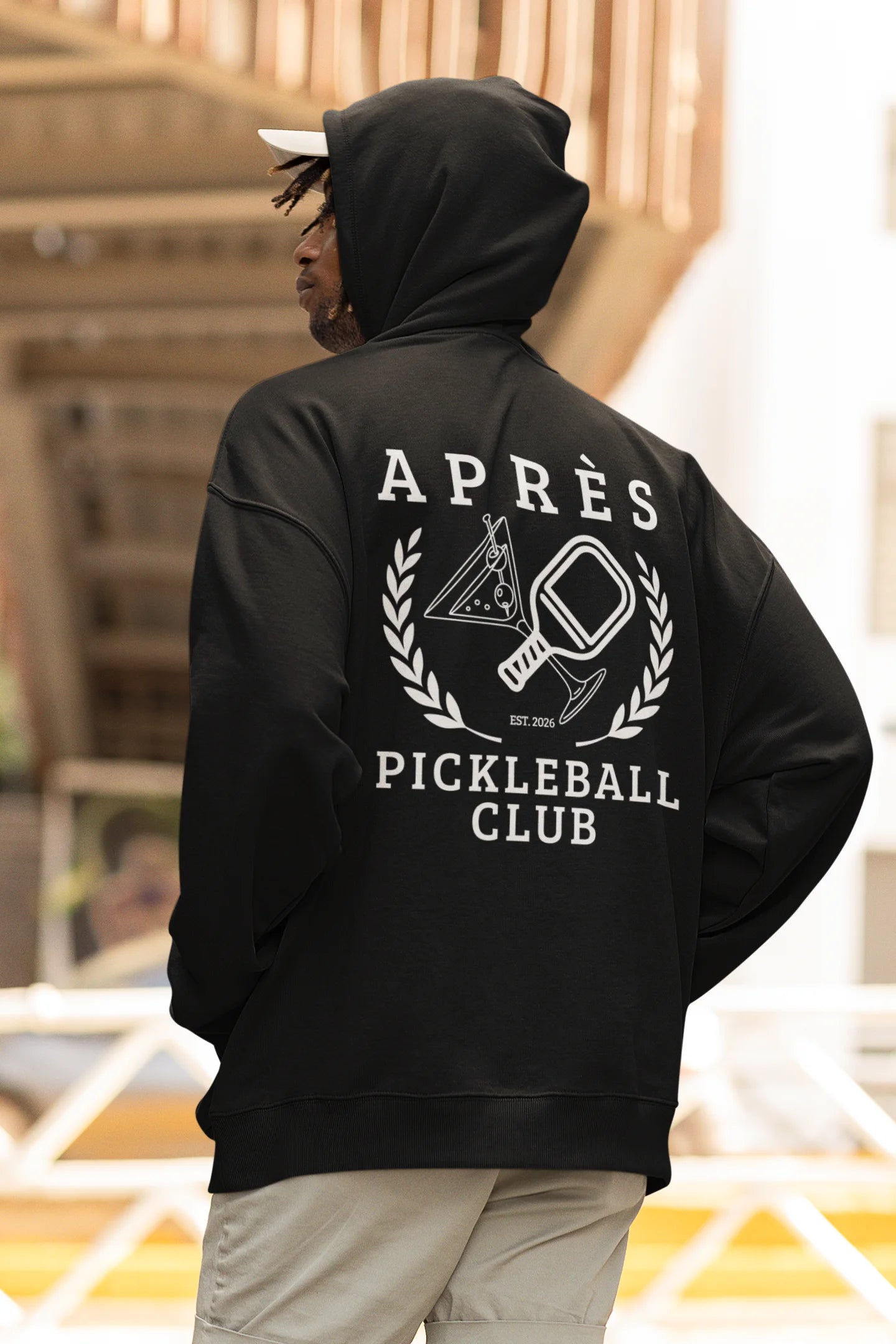 Funny Pickleball Hoodie Person wearing a black hoodie with 'Apres Pickleball Club' design on the back.
