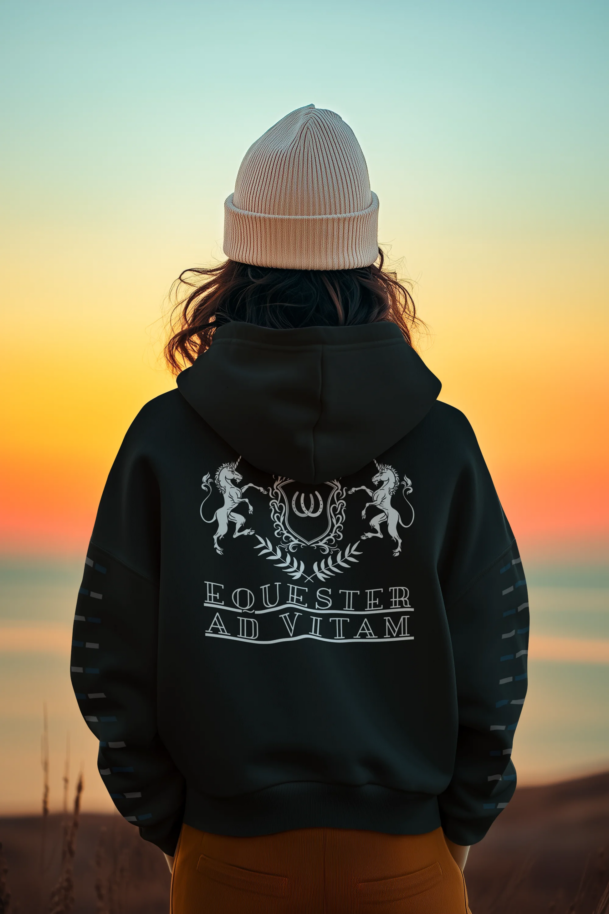 Person wearing a black hoodie with text and graphics, standing against a sunset sky.
