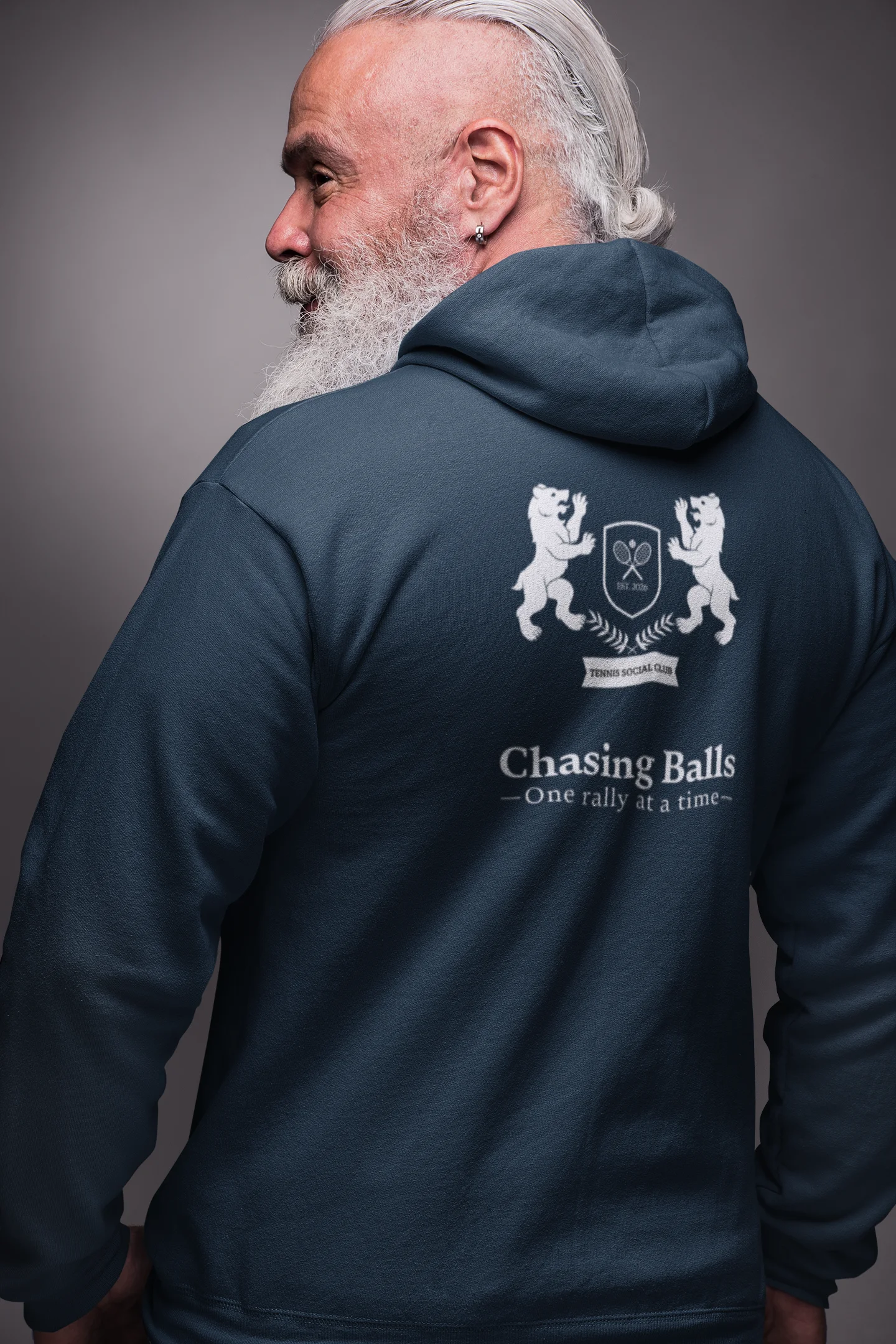 Man wearing a navy hoodie with a logo and text on the back, standing against a gray background.