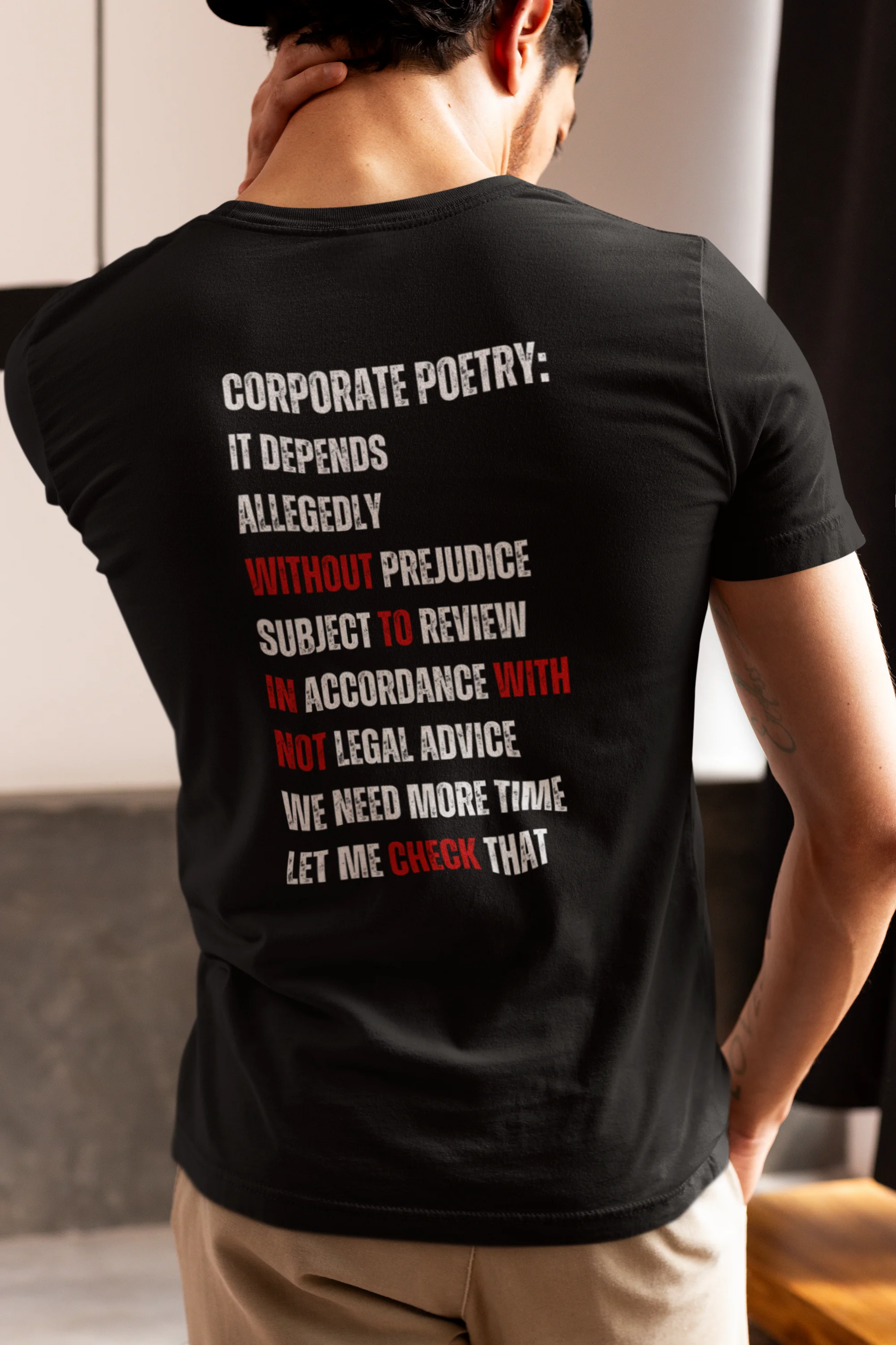 Person wearing a black t-shirt with text on the back, standing indoors.