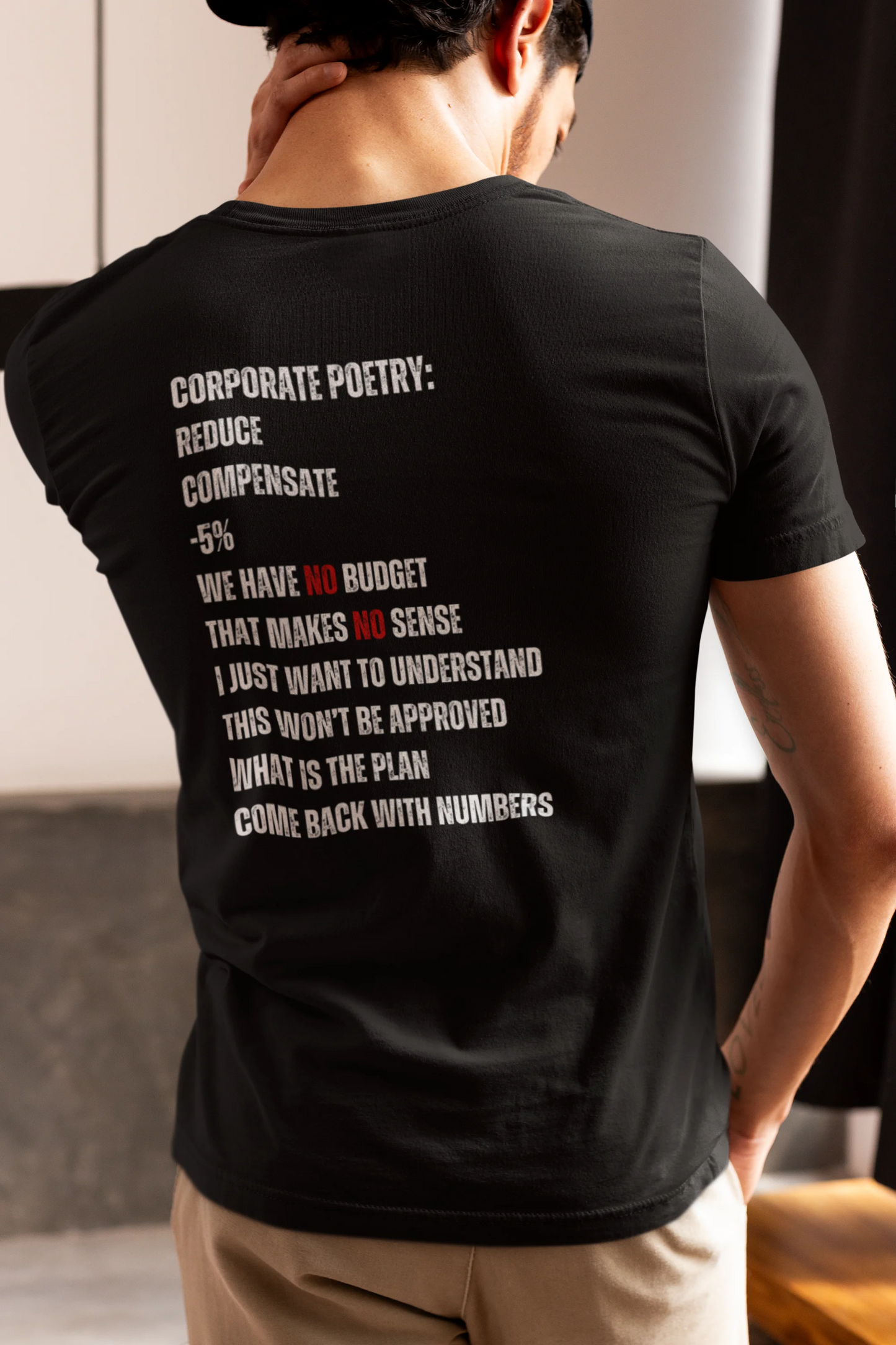 Finance Controller Shirt Person wearing a black t-shirt with text on the back, standing indoors.