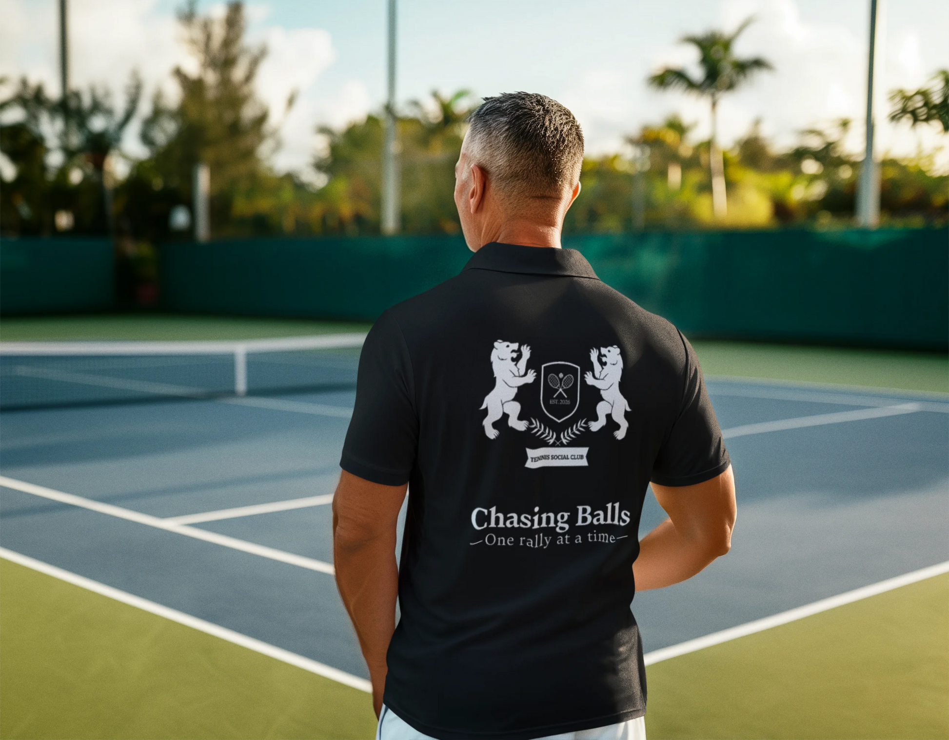Person wearing a black polo shirt with a logo and text on a tennis court