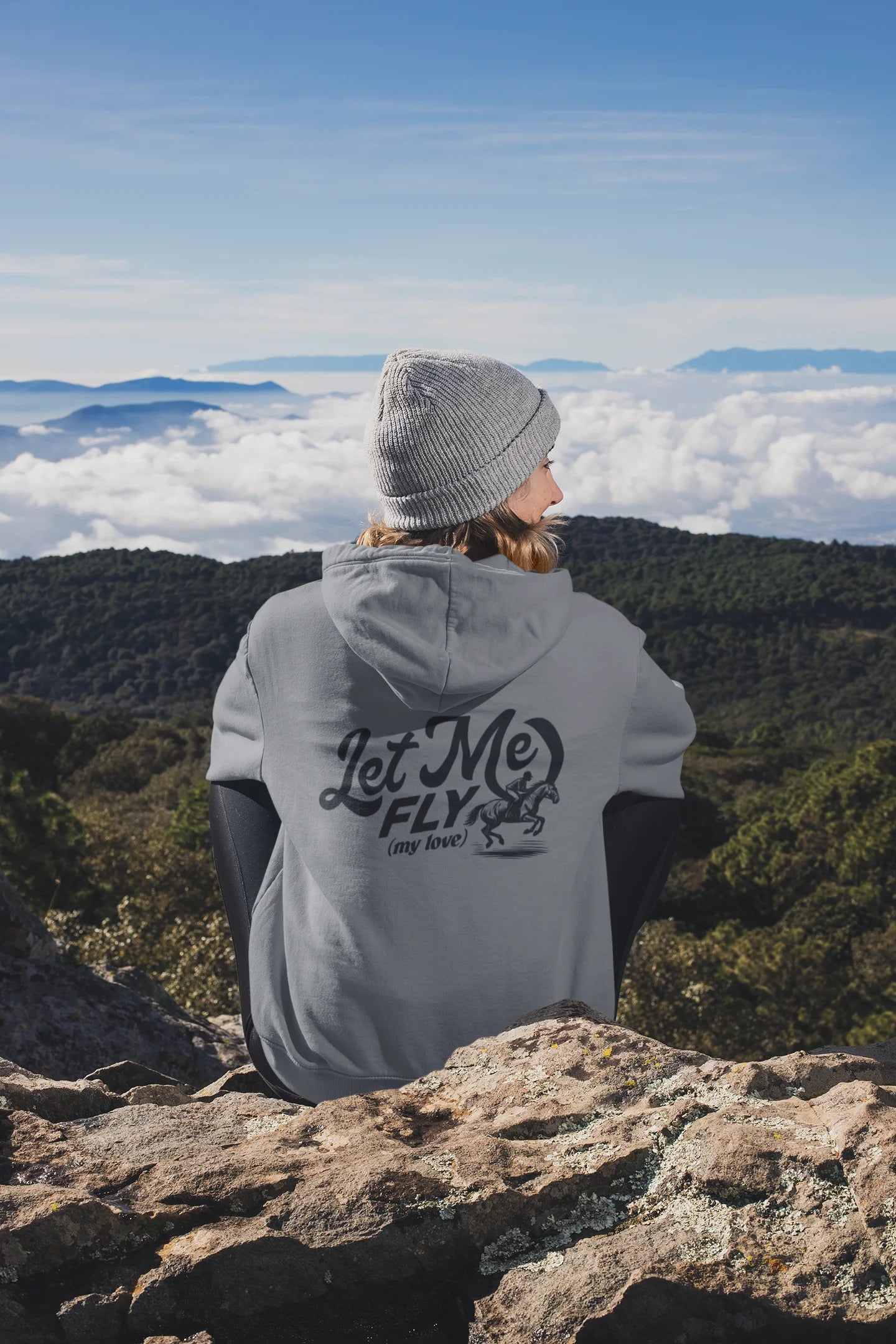 Barn to street Person wearing a hoodie with 'Let Me Fly' text, sitting on a mountain overlooking a scenic landscape.