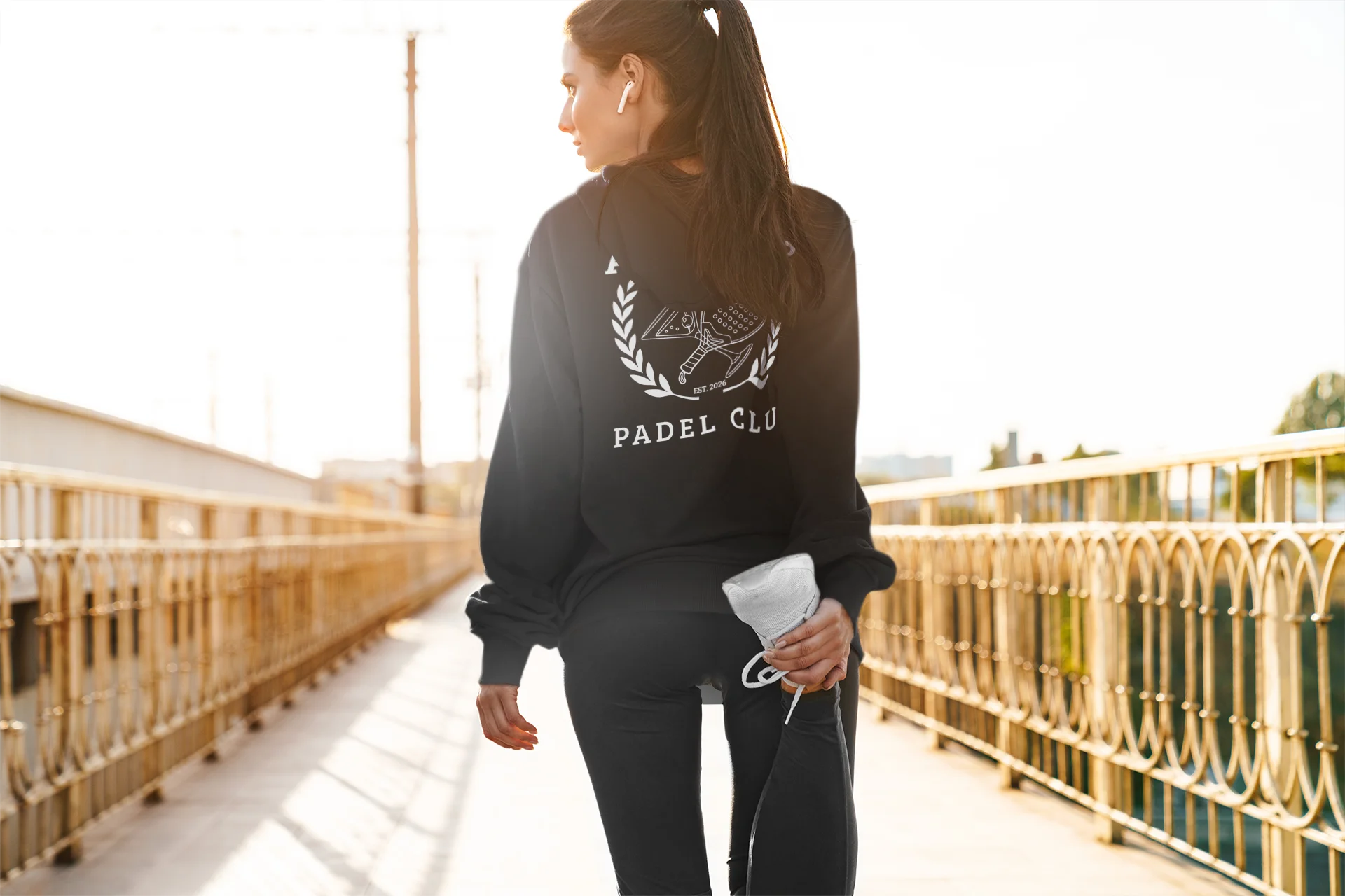 Hoodie Padel Woman in black athletic wear with 'PADEL CLU' branding on a bridge