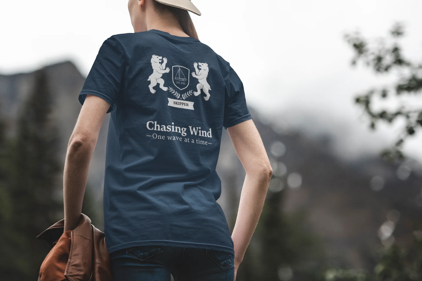 Sailing T-Shirt Person wearing a blue t-shirt with a logo and text, standing outdoors with a blurred natural background