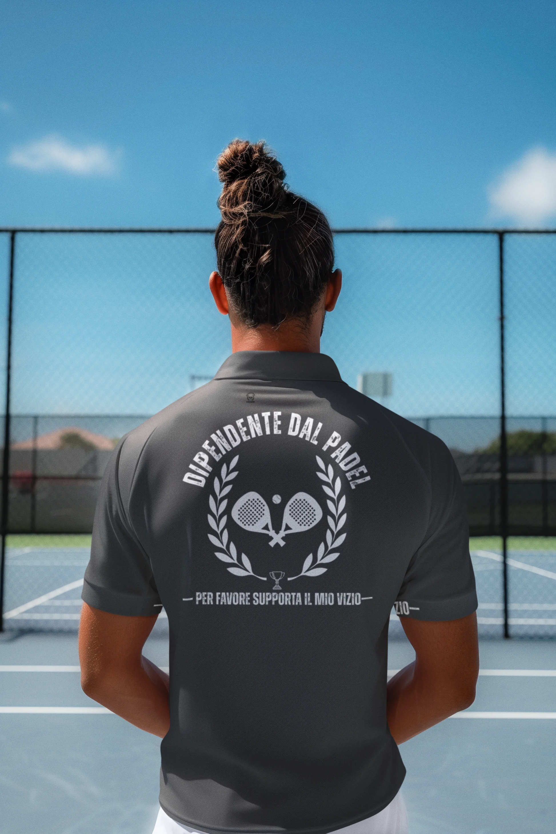 Person wearing a gray polo shirt with a logo and text on the back, standing on a tennis court.