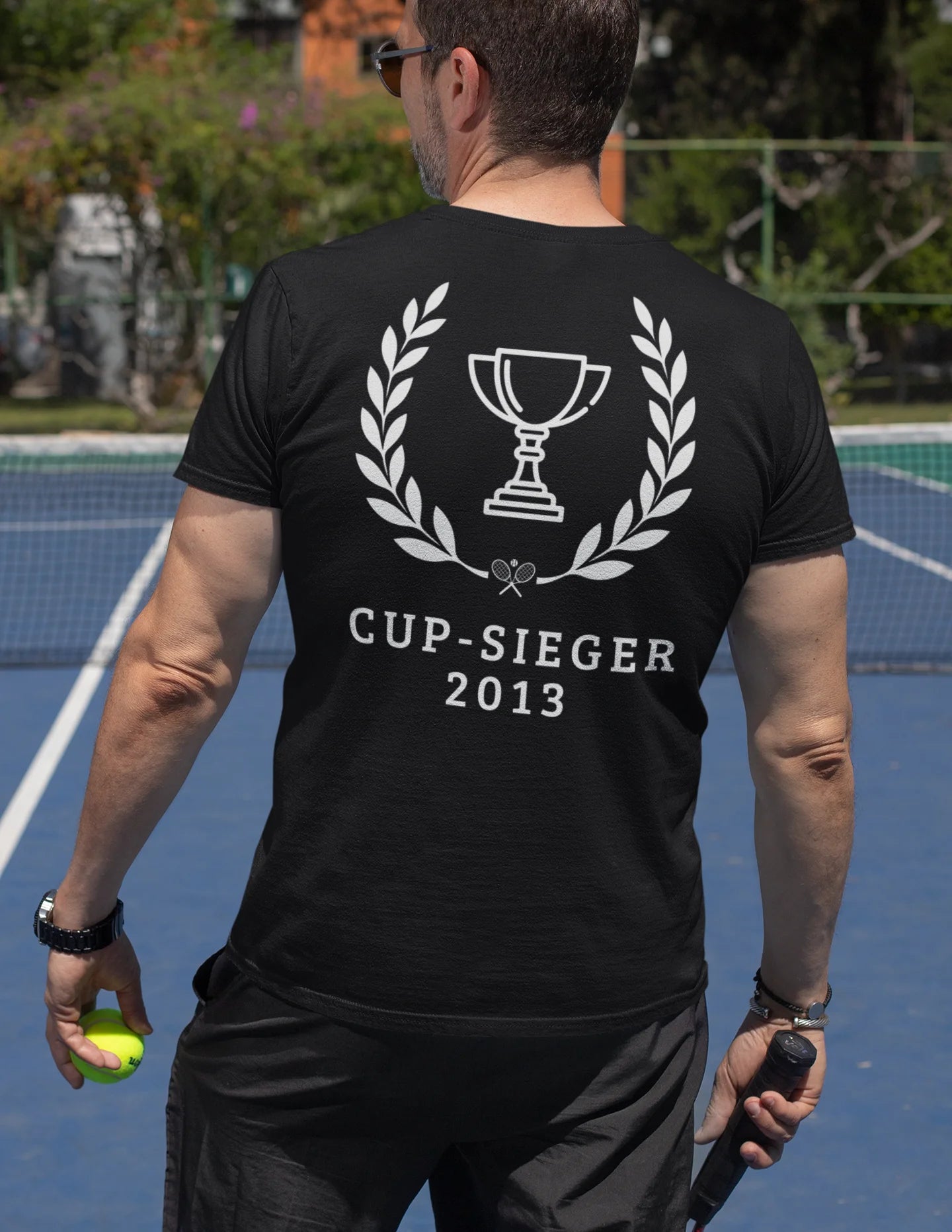 Xutos More than tennis Person wearing a black t-shirt with 'Cup-Sieger 2013' design on a tennis court.