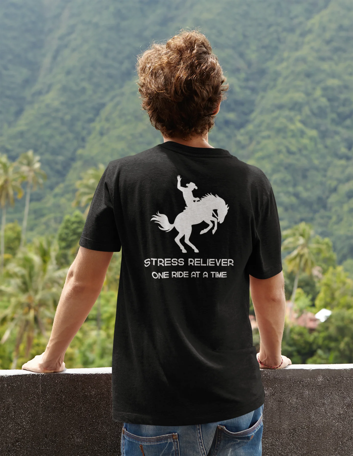 Person wearing a black t-shirt with a graphic and text, standing against a scenic mountain backdrop.