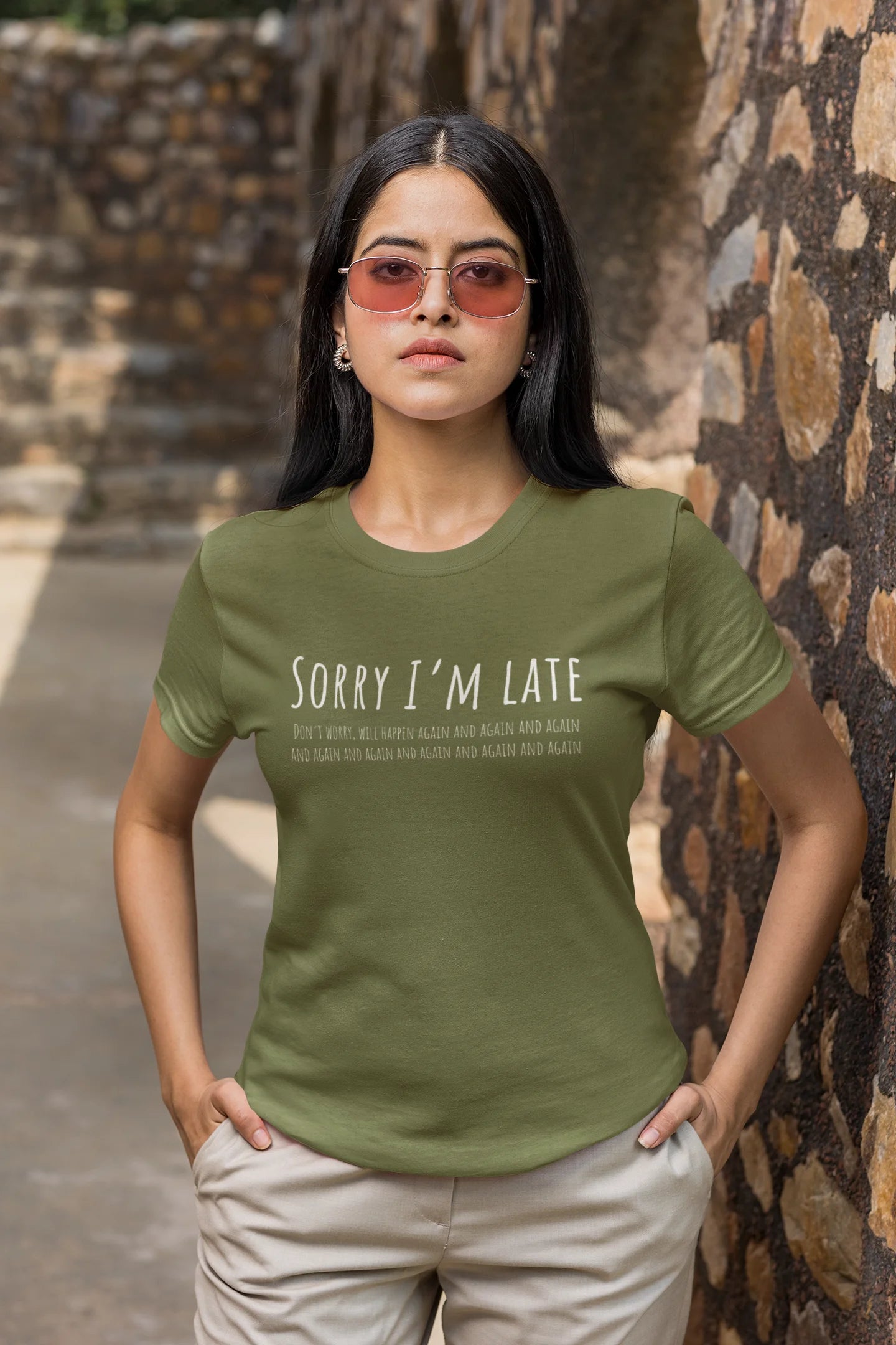 Woman wearing a green t-shirt with text standing in front of a stone wall.