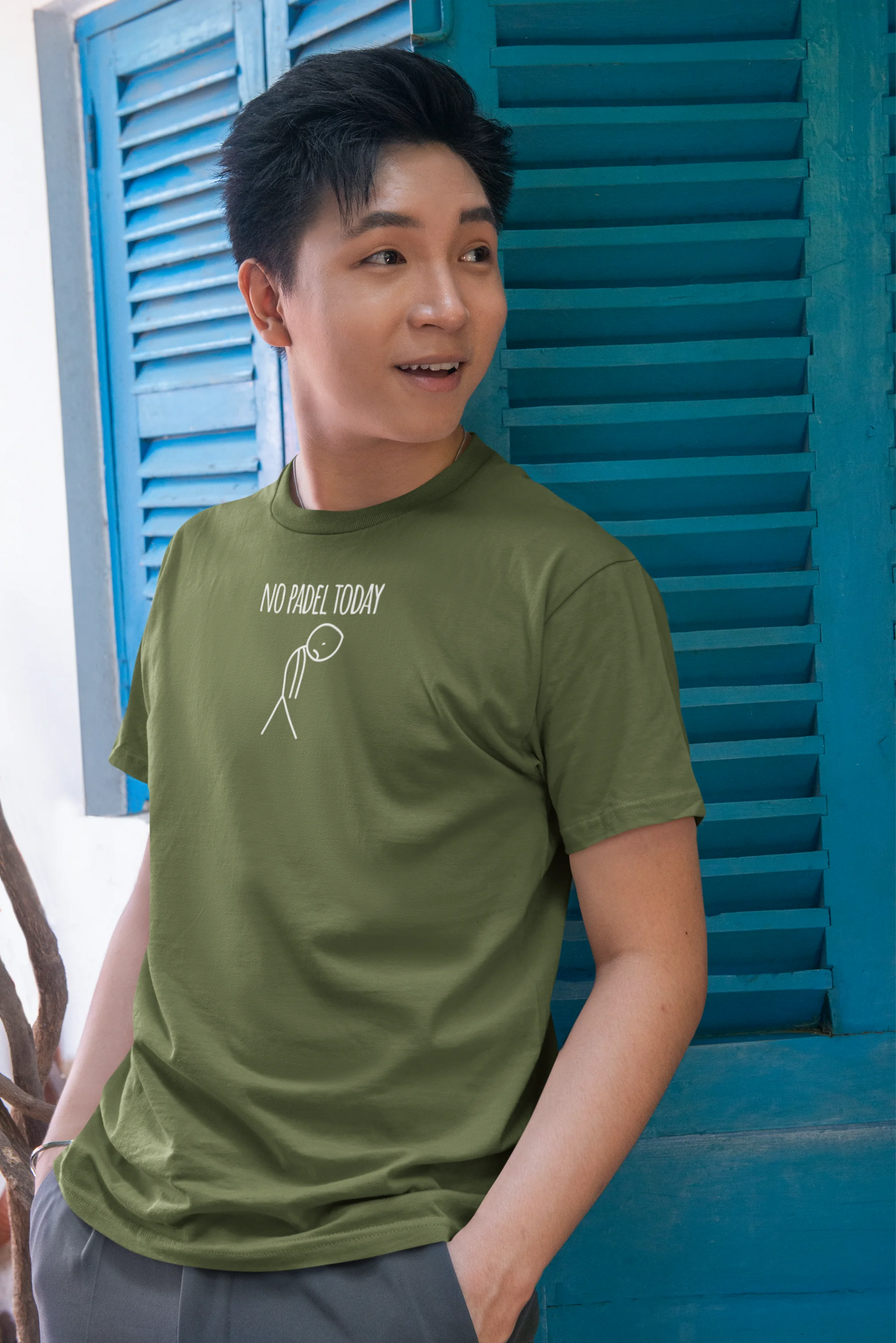 Person wearing a green t-shirt with text and graphics, standing in front of blue shutters.
