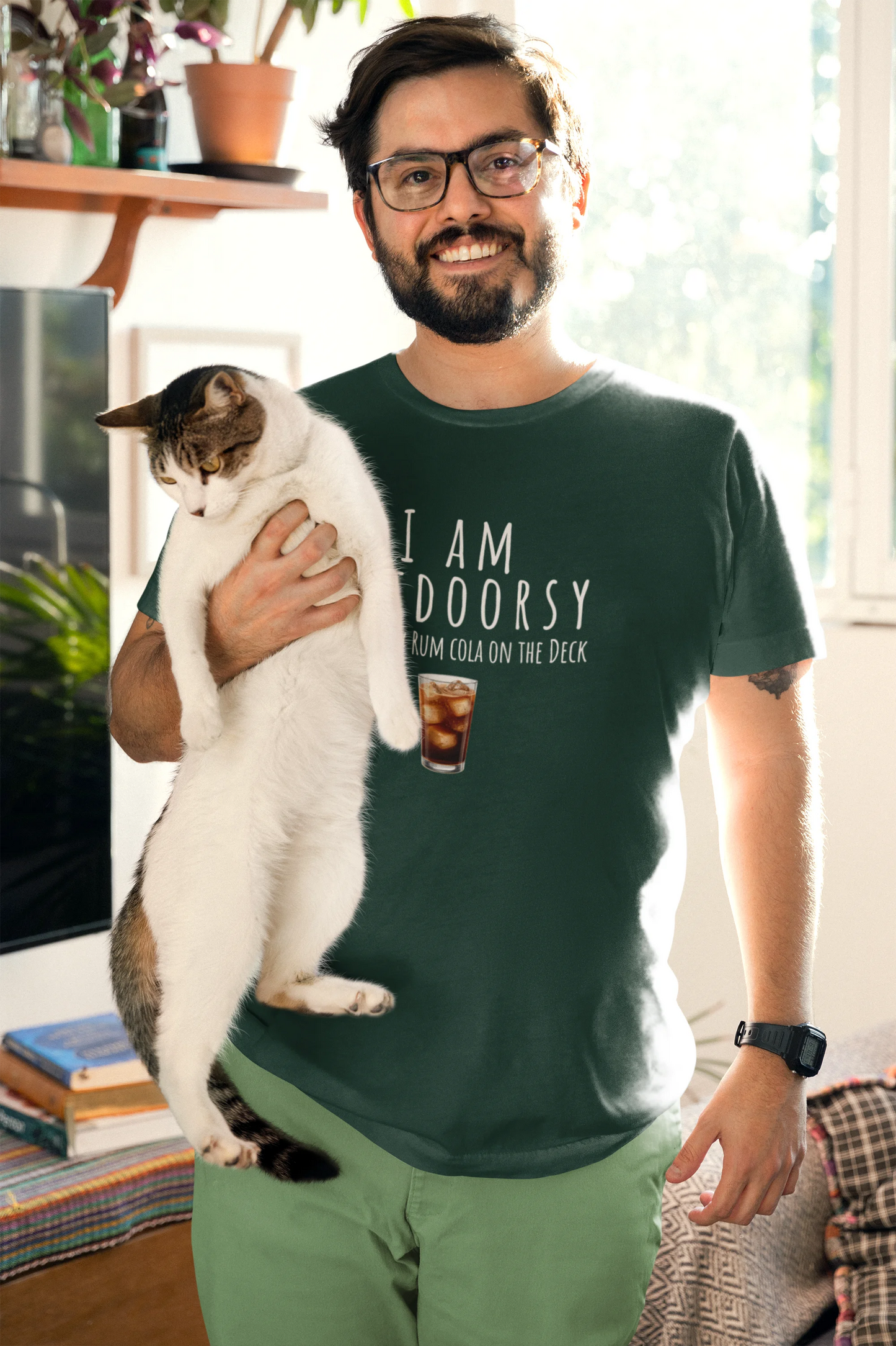 Man holding a cat wearing a green t-shirt with text in a living room.