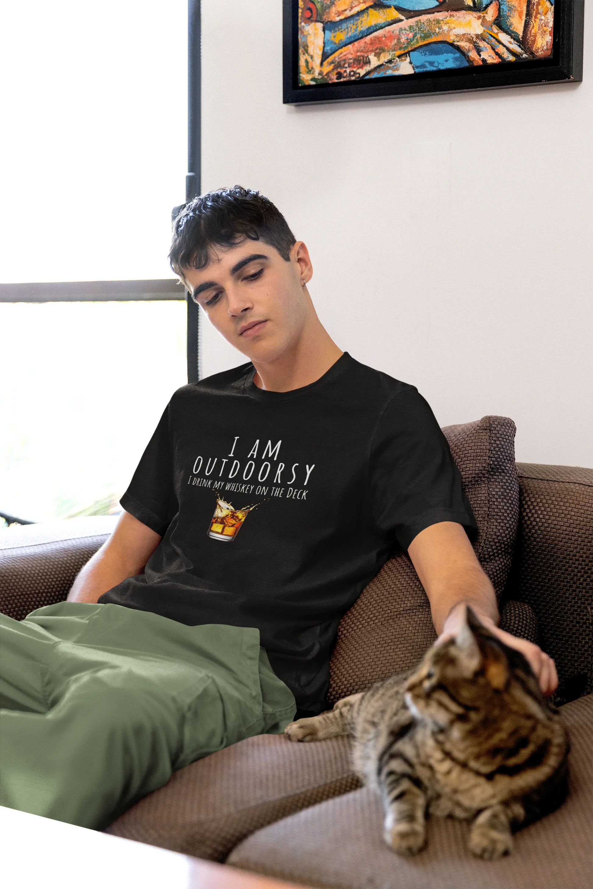 Person wearing a black t-shirt with 'I AM OUTDOORSY' text, sitting on a couch with a cat.