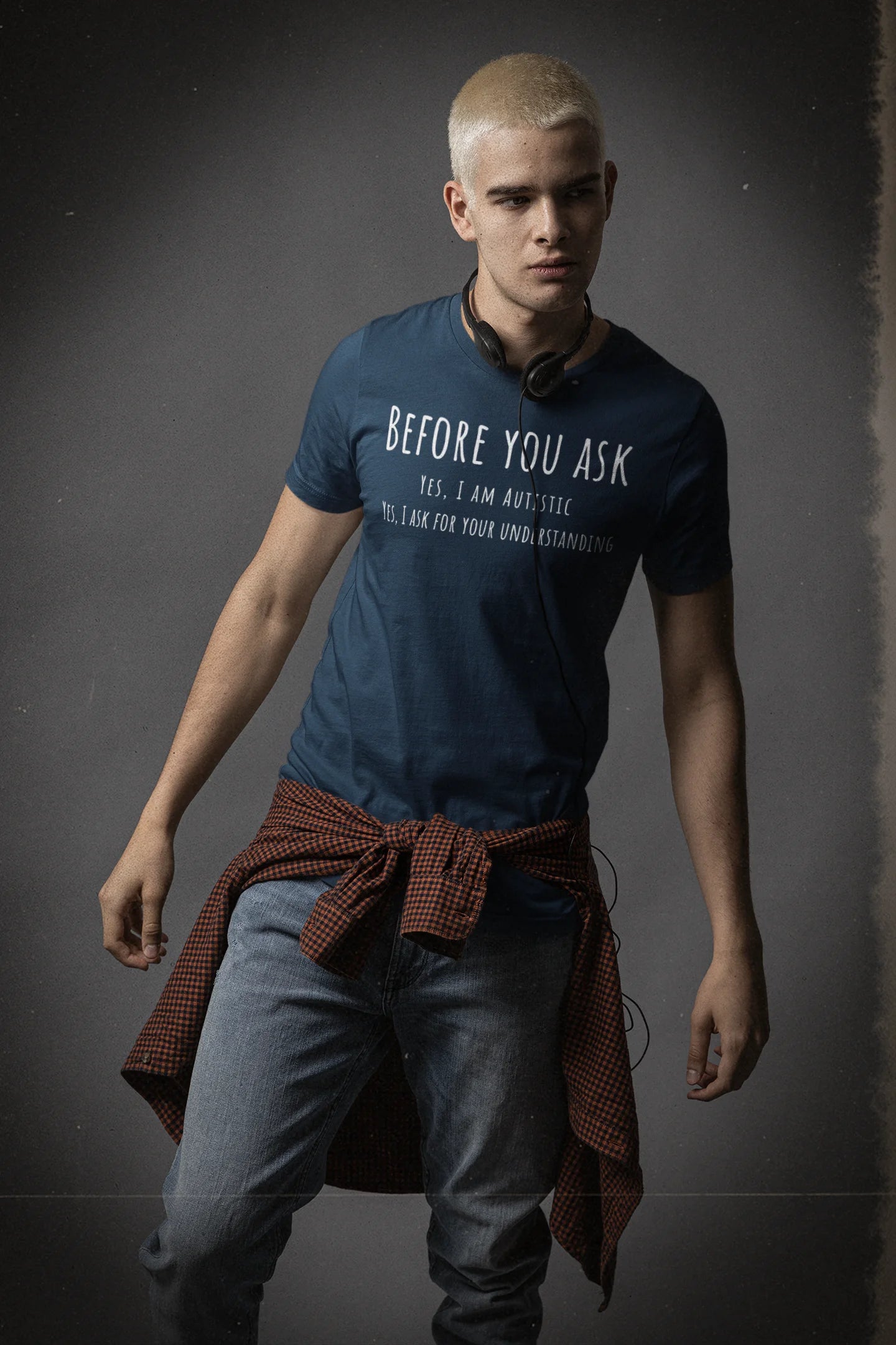 Man wearing a blue t-shirt with text and a brown jacket over his shoulder against a dark background