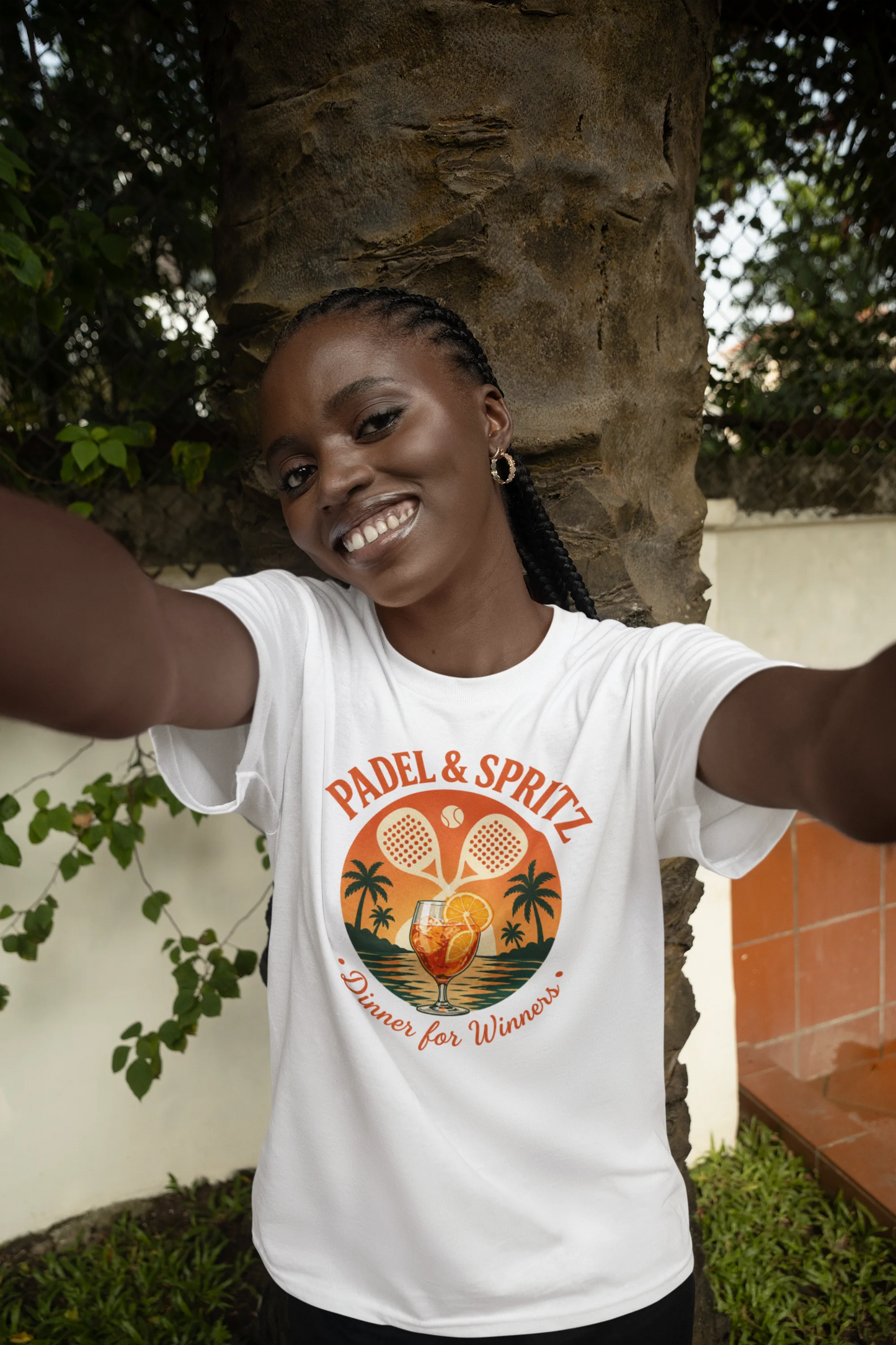 Padel Aperol T-Shirt Woman wearing a 'Padel & Spritz' t-shirt with a tropical design, standing outdoors.