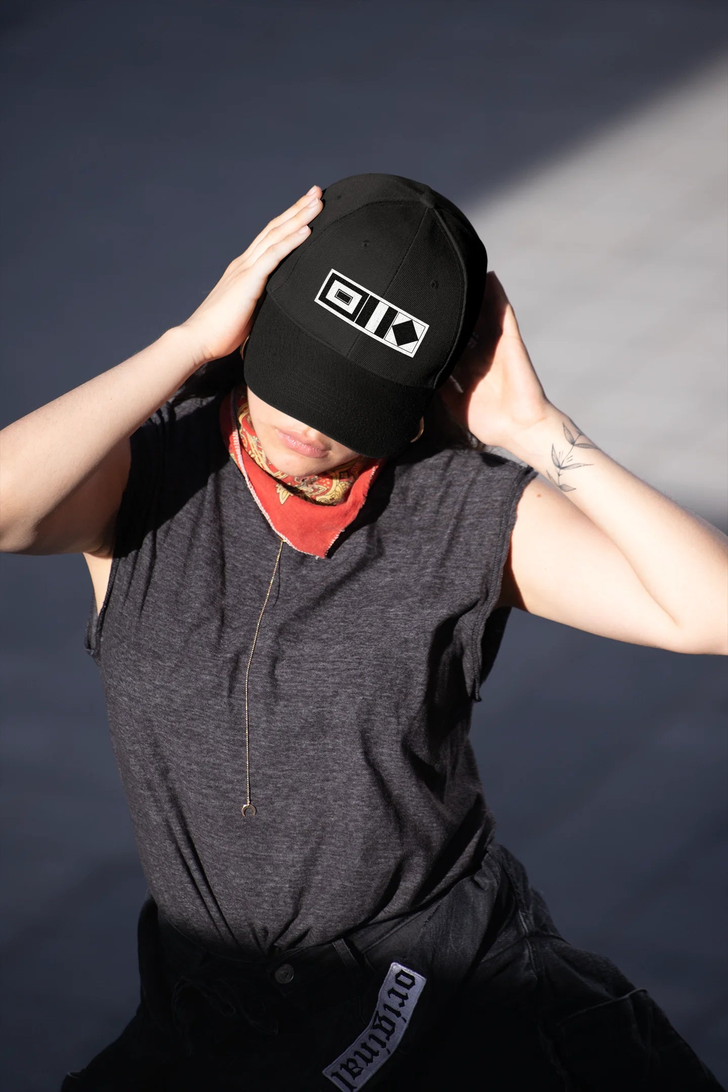 Sailing Cap Person wearing a black cap with a logo, gray sleeveless shirt, and dark pants against a dark background.