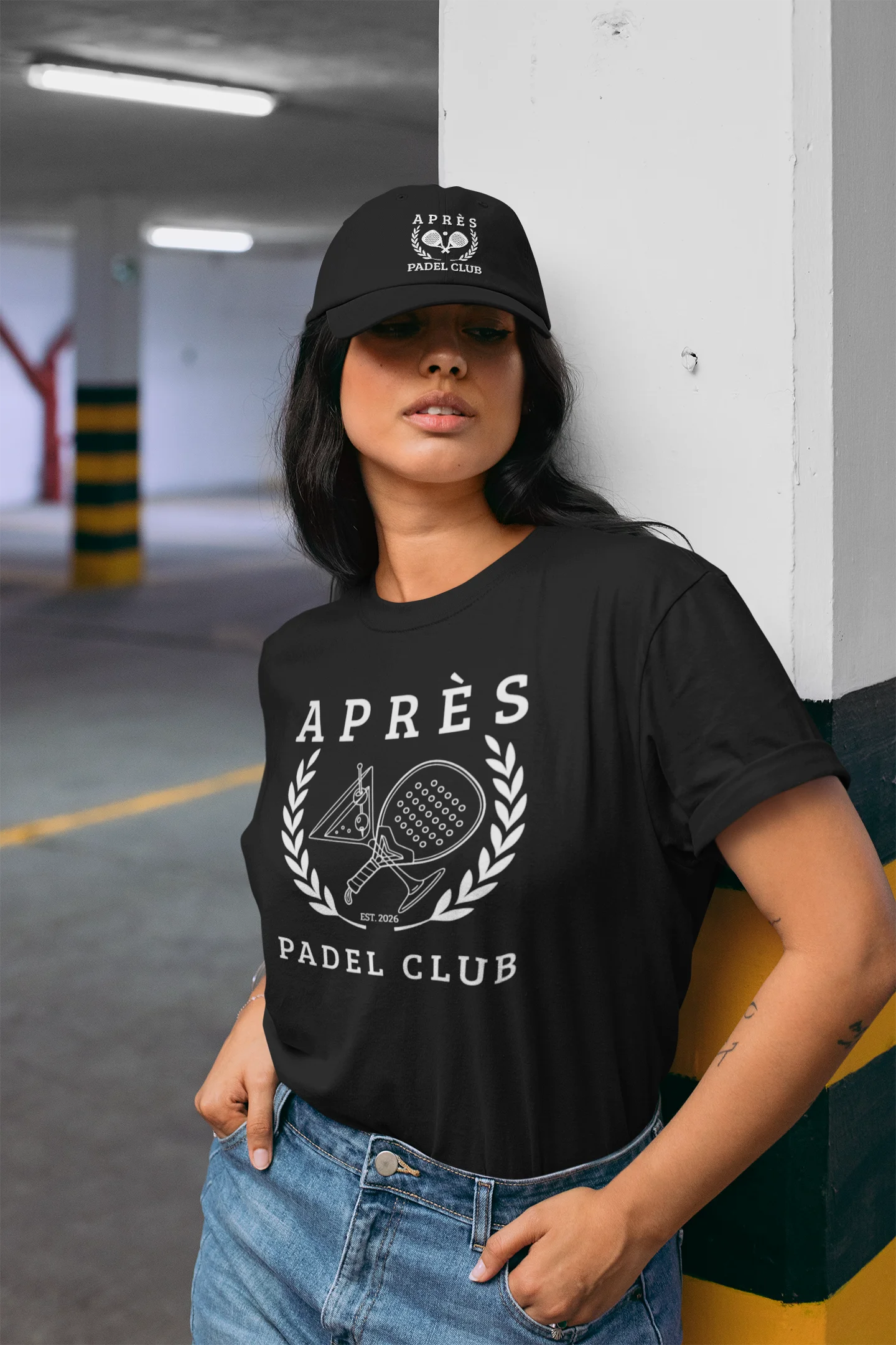 Padel Cap Person wearing a black t-shirt with 'Apres Padel Club' design and a matching cap in an indoor setting.