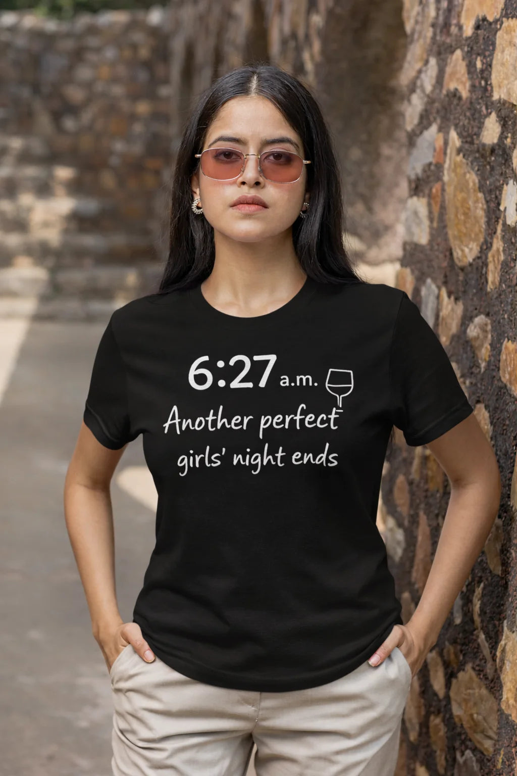 Woman wearing a black t-shirt with text standing against a stone wall.