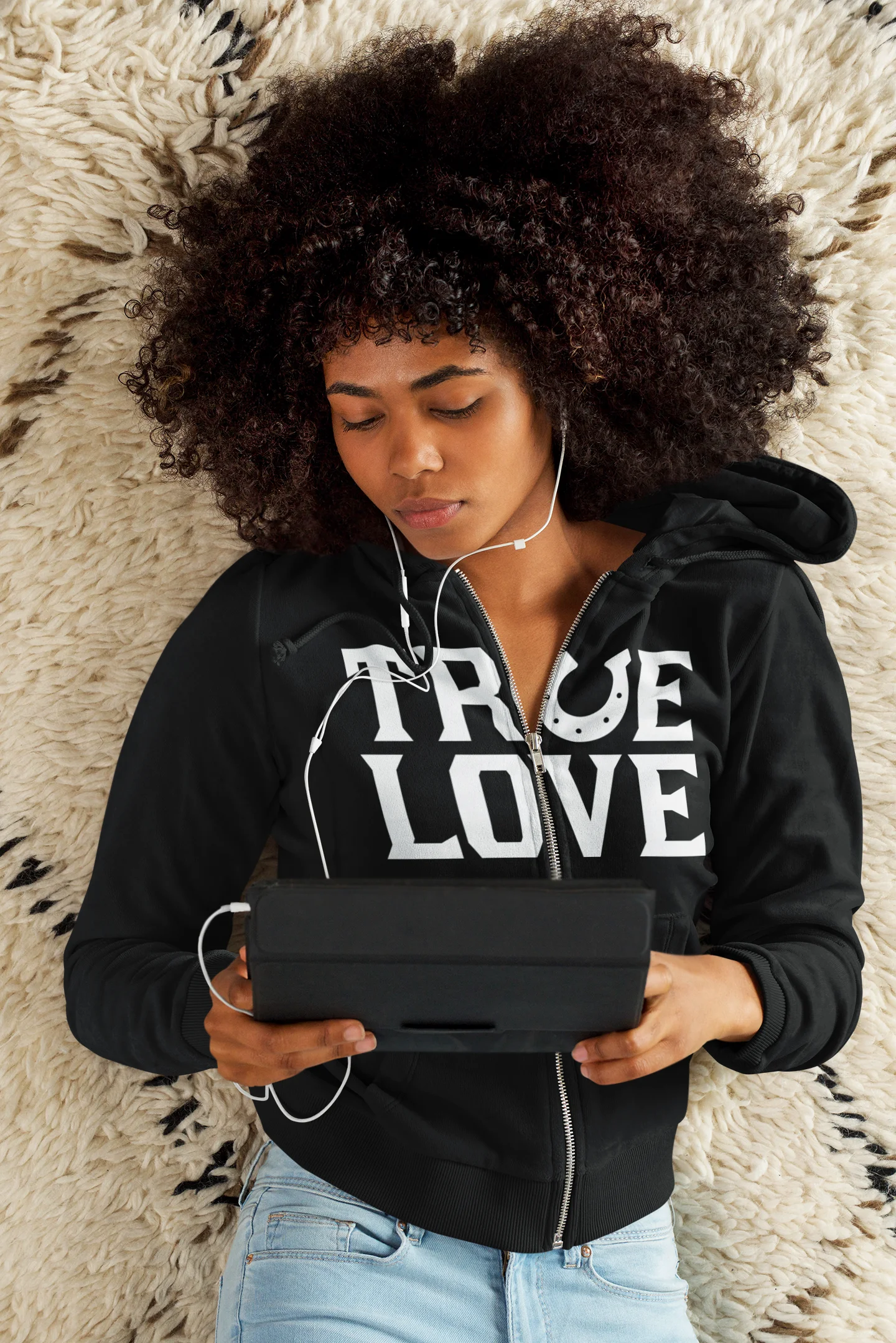 True love horseshoe hoodie Person wearing a black hoodie with 'TRUE LOVE' text, using a tablet on a textured surface.