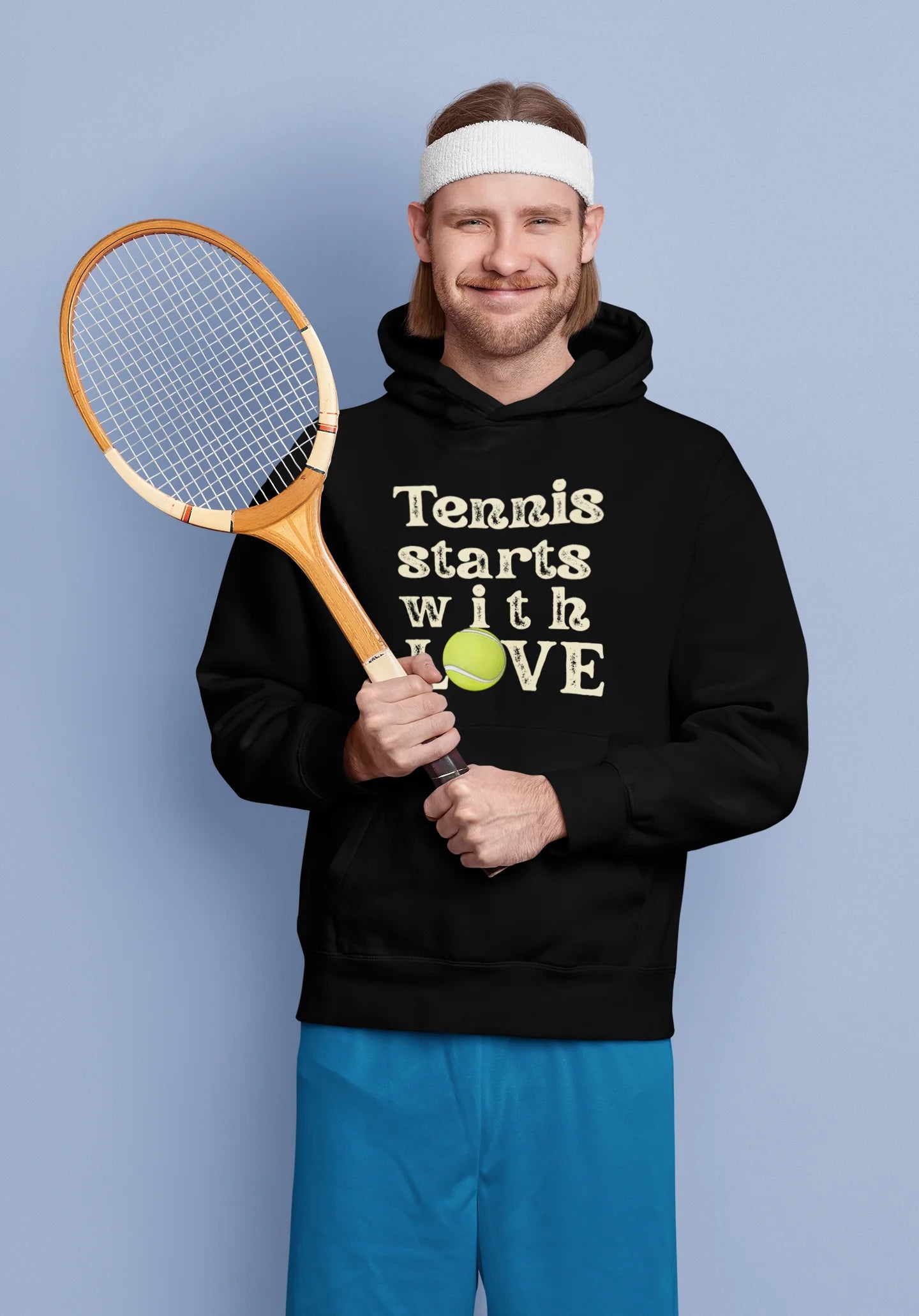 Man holding a tennis racket and wearing a hoodie with 'Tennis starts with LOVE' text on a blue background