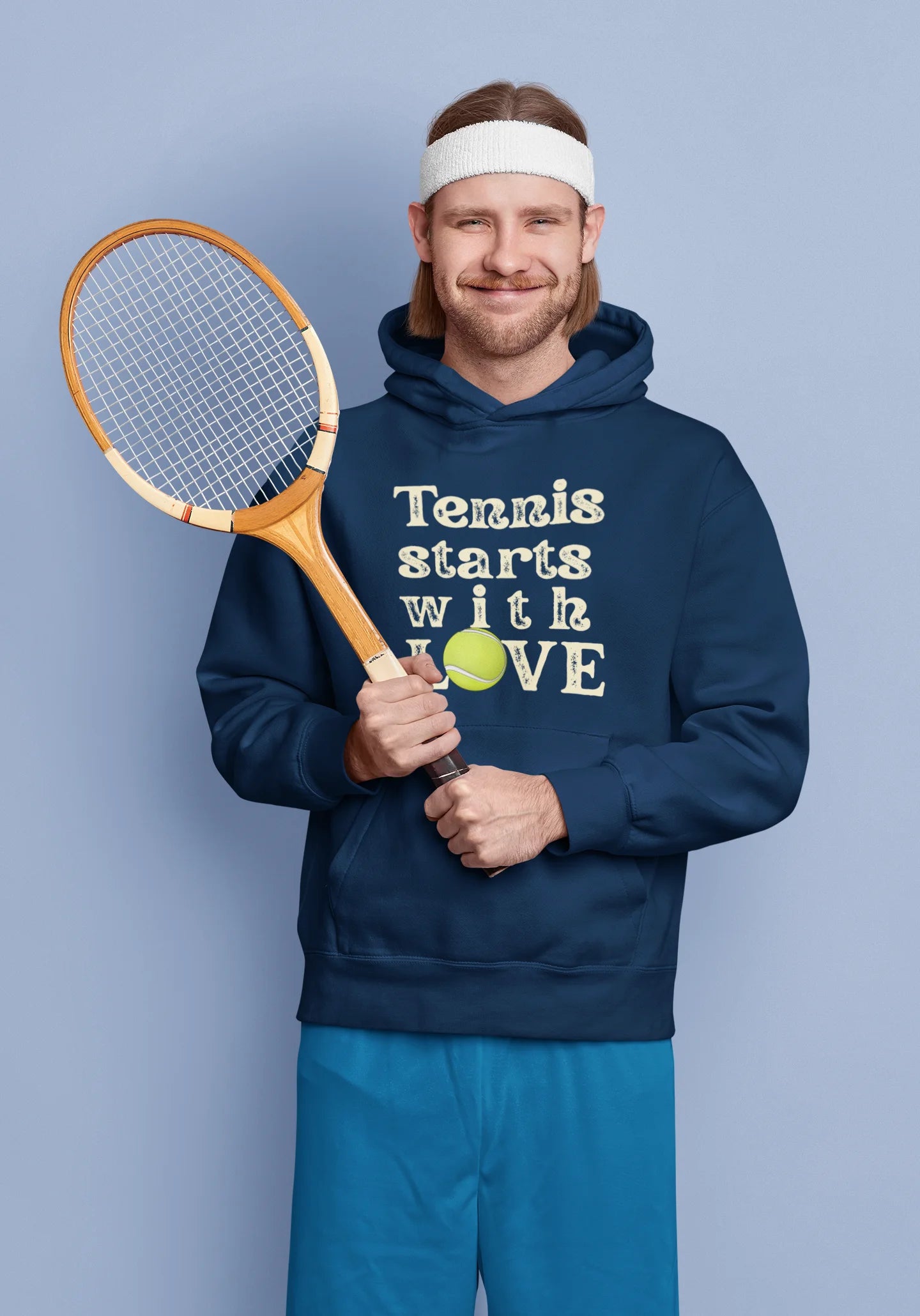 Man holding a tennis racket and a ball, wearing a navy hoodie with 'Tennis starts with LOVE' text, on a light blue background.