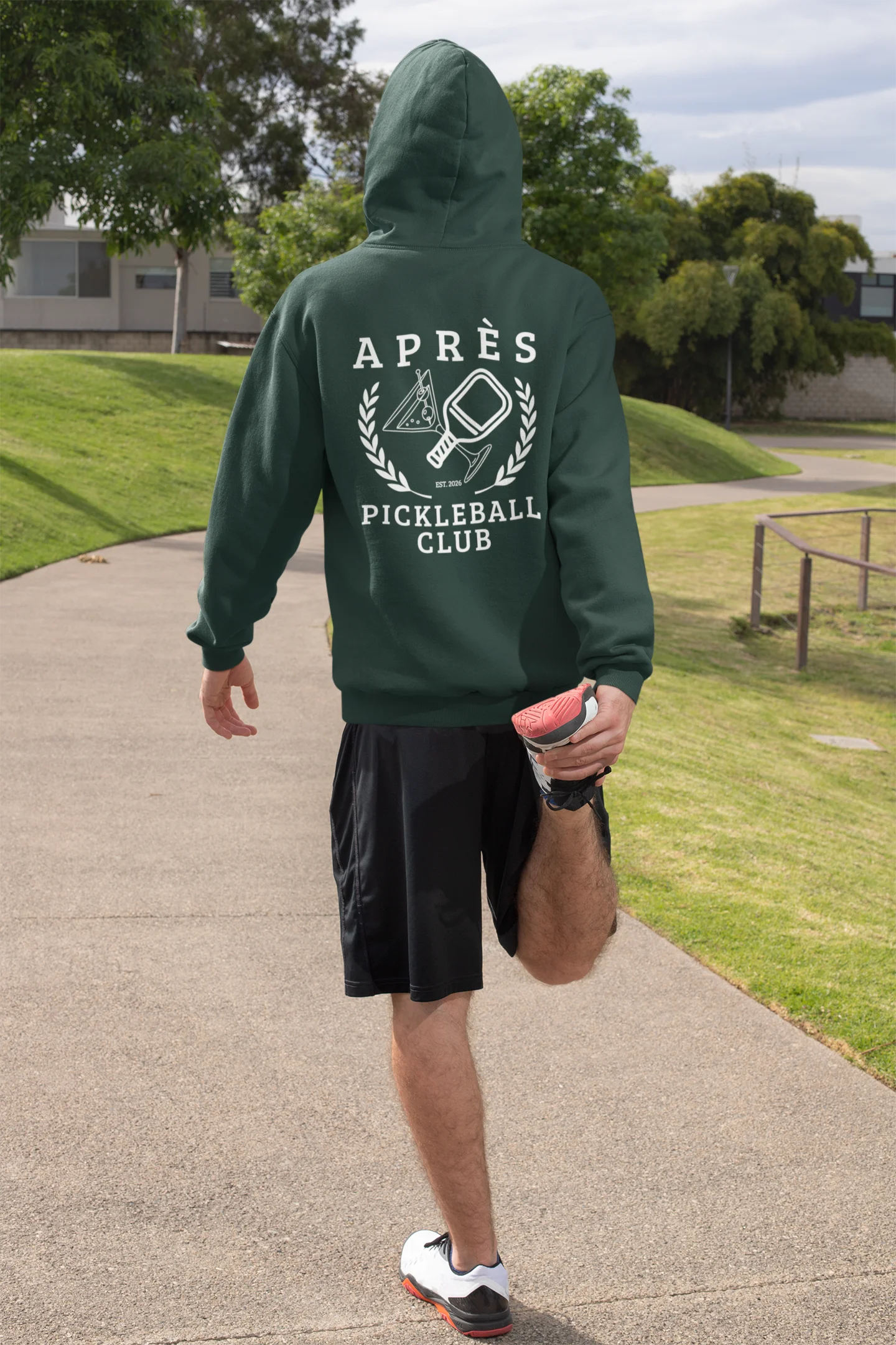 Funny Pickleball Hoodie Person wearing a green hoodie with 'Apres Pickleball Club' text, stretching outdoors.