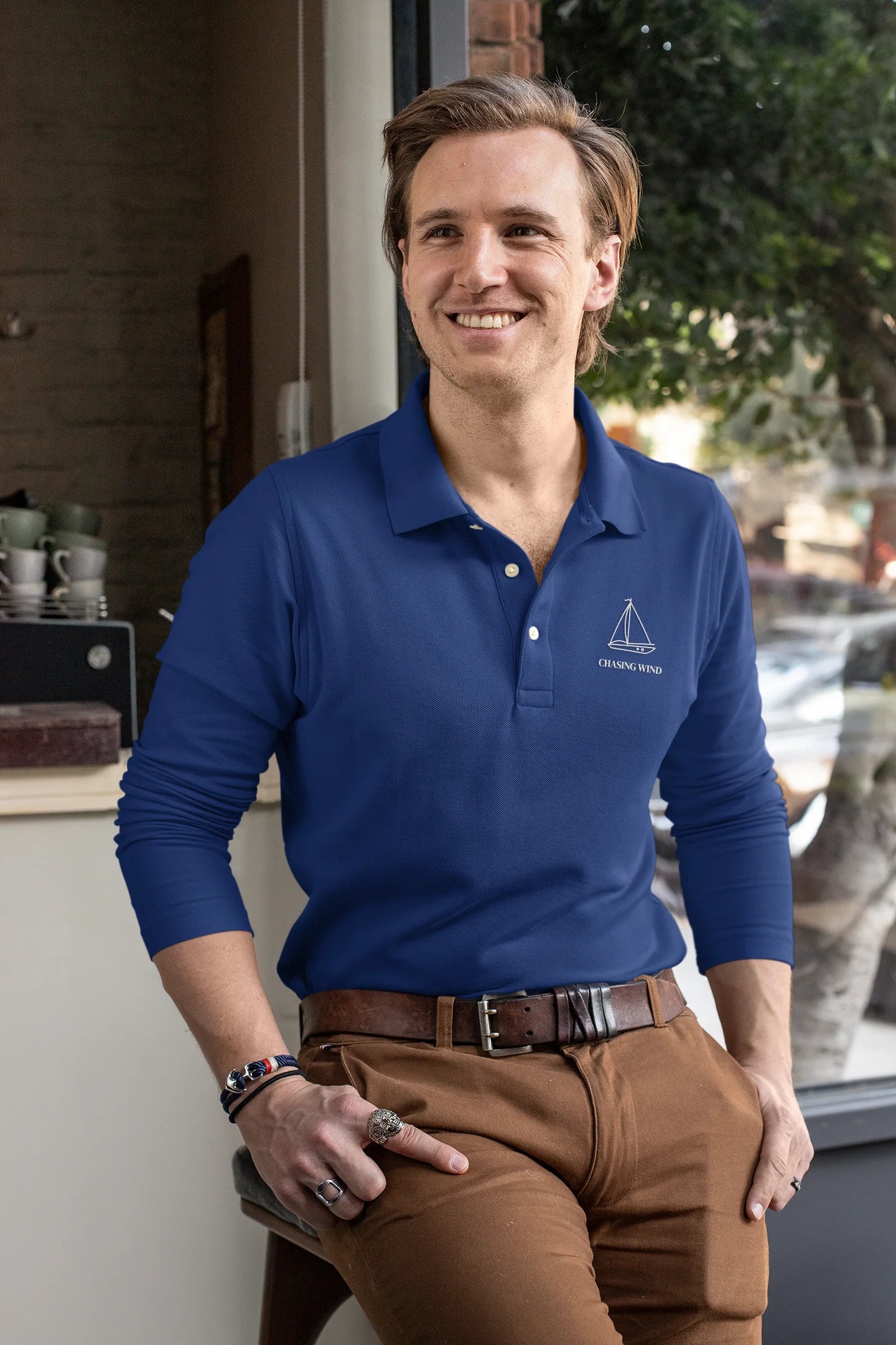 Sailing Polo Shirt Man wearing a blue polo shirt with a logo, sitting in a casual setting.