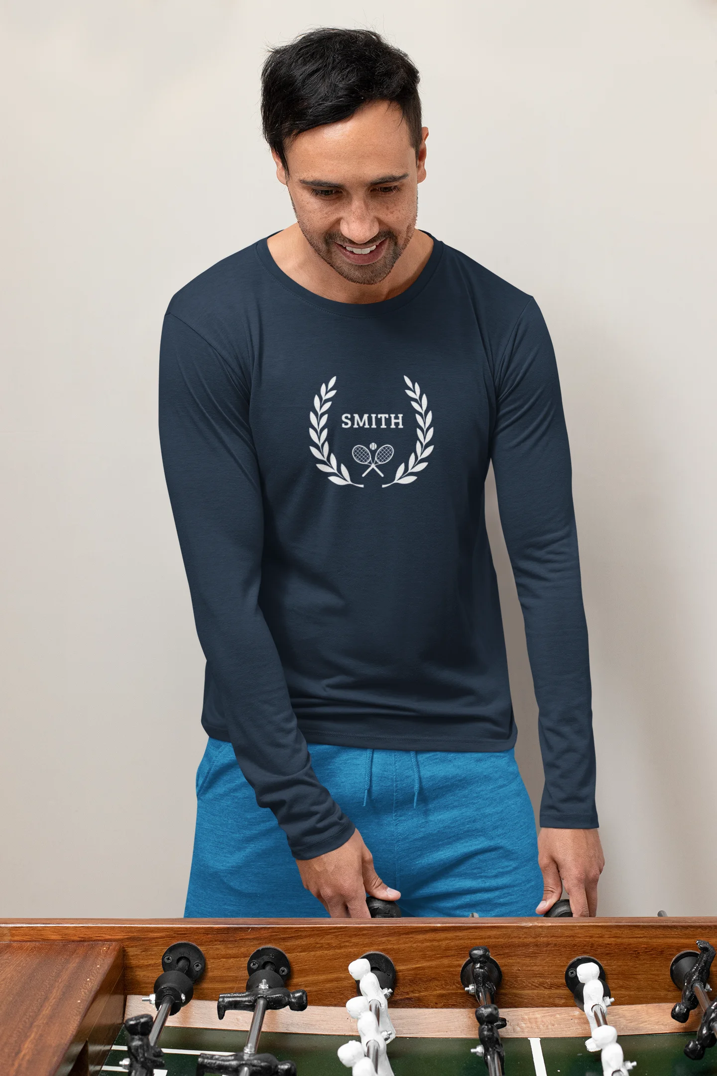 long sleeve tennis shirt Man wearing a navy long-sleeve shirt with 'Smith' logo on a foosball table.
