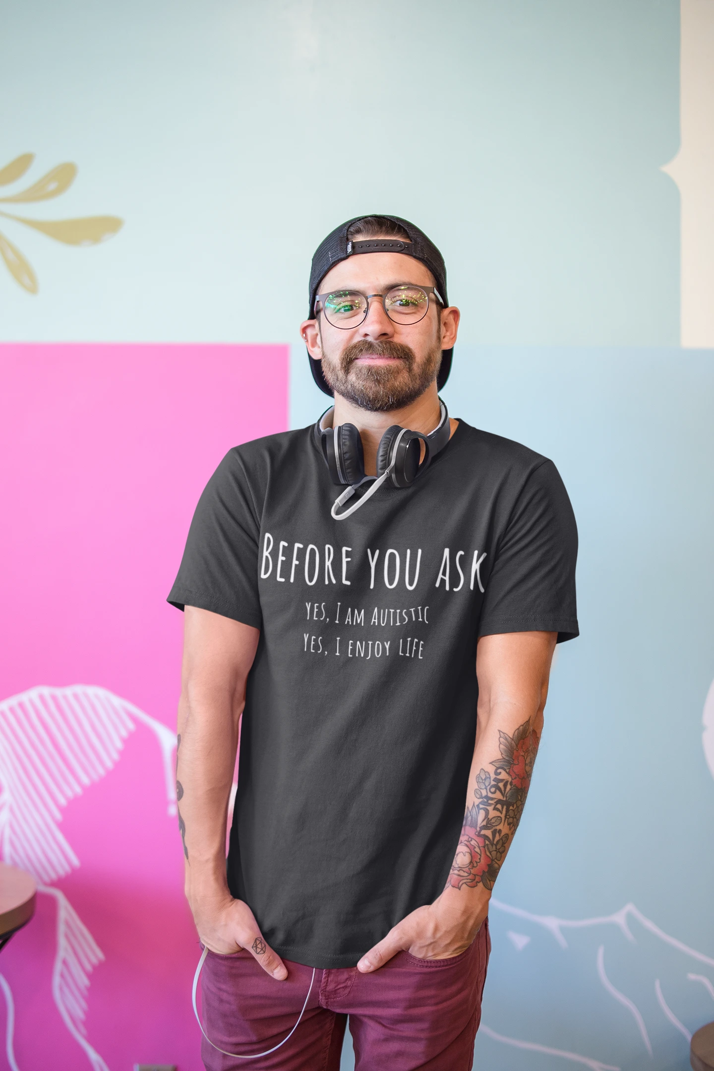 Man wearing a black t-shirt with text, standing against a colorful wall.