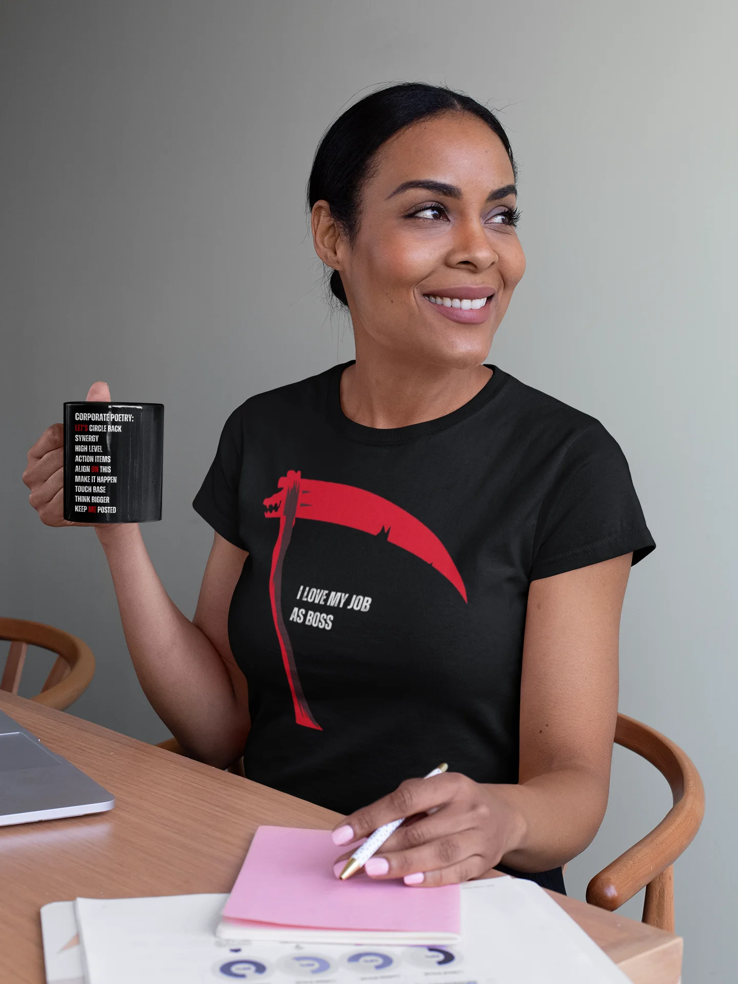 Woman holding a mug and wearing a black t-shirt with a graphic design, sitting at a table.