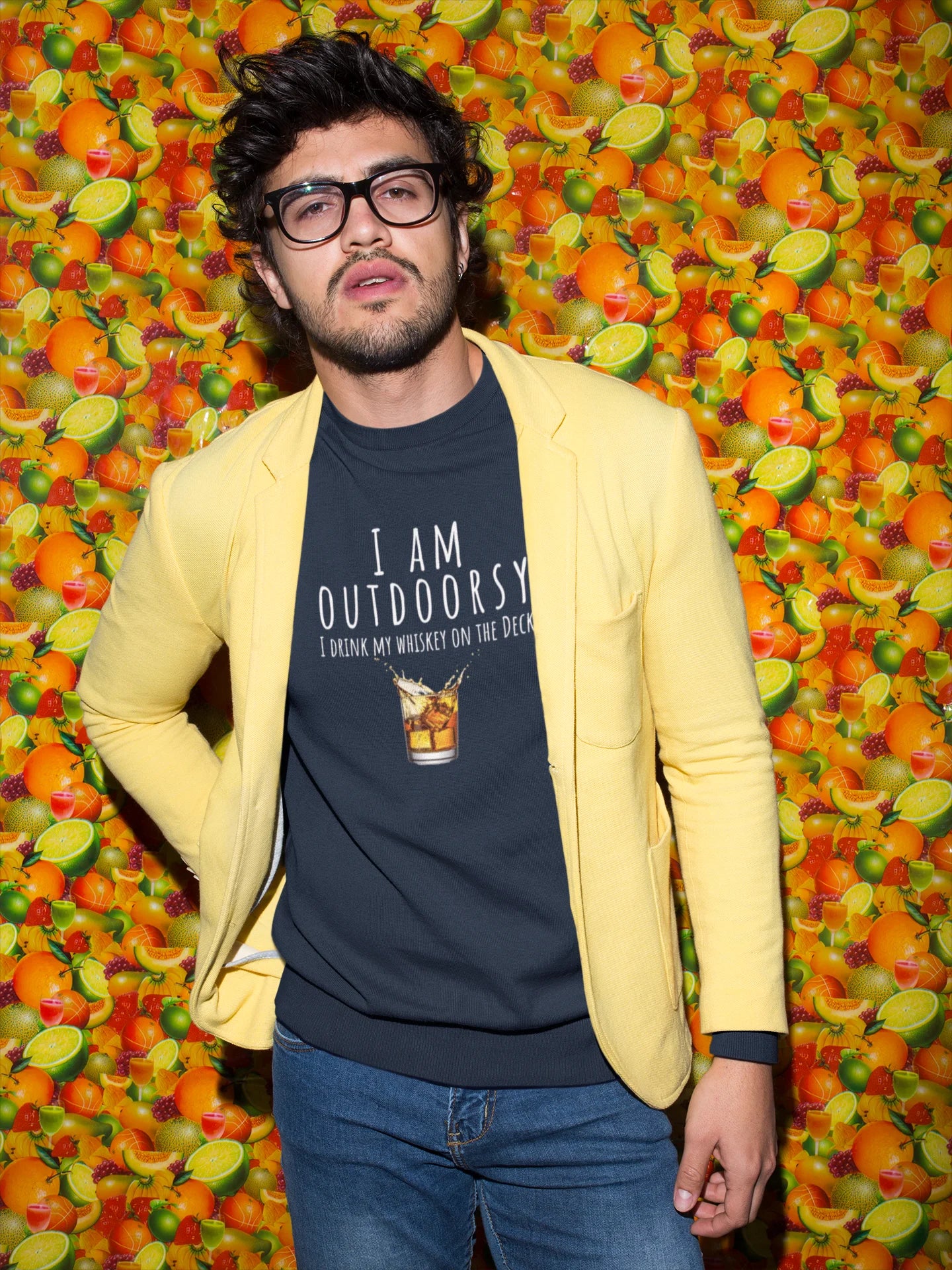 Person wearing a yellow blazer over a navy t-shirt with text, standing against a colorful fruit background