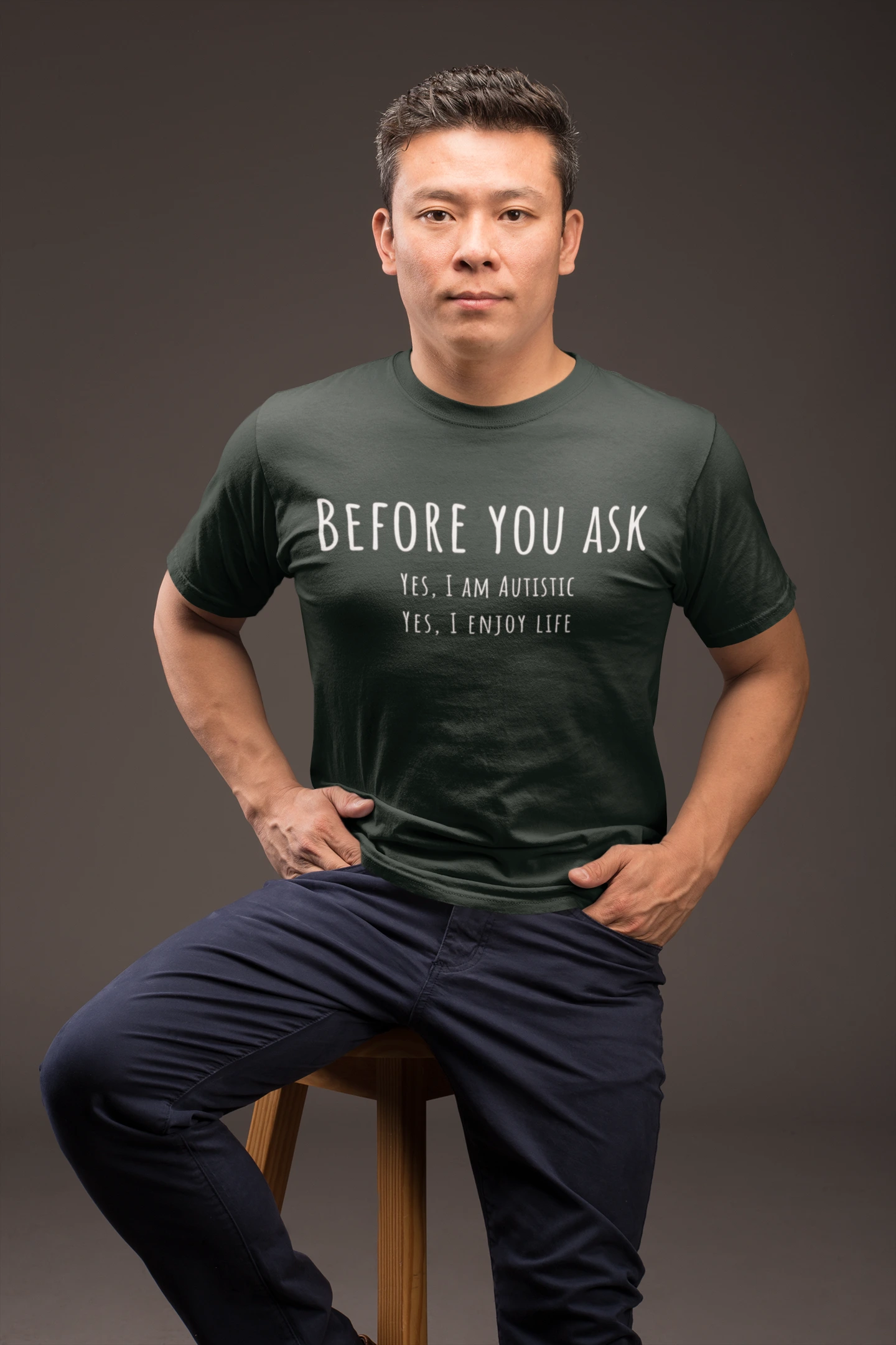 Man wearing a dark green t-shirt with text, sitting on a stool against a dark background