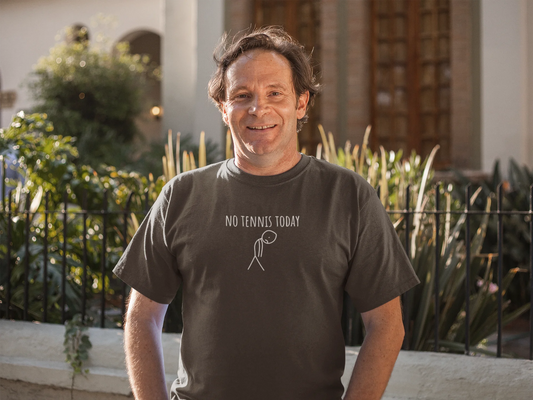 Man wearing a 'No Tennis Today' t-shirt standing outdoors with plants and a building in the background.