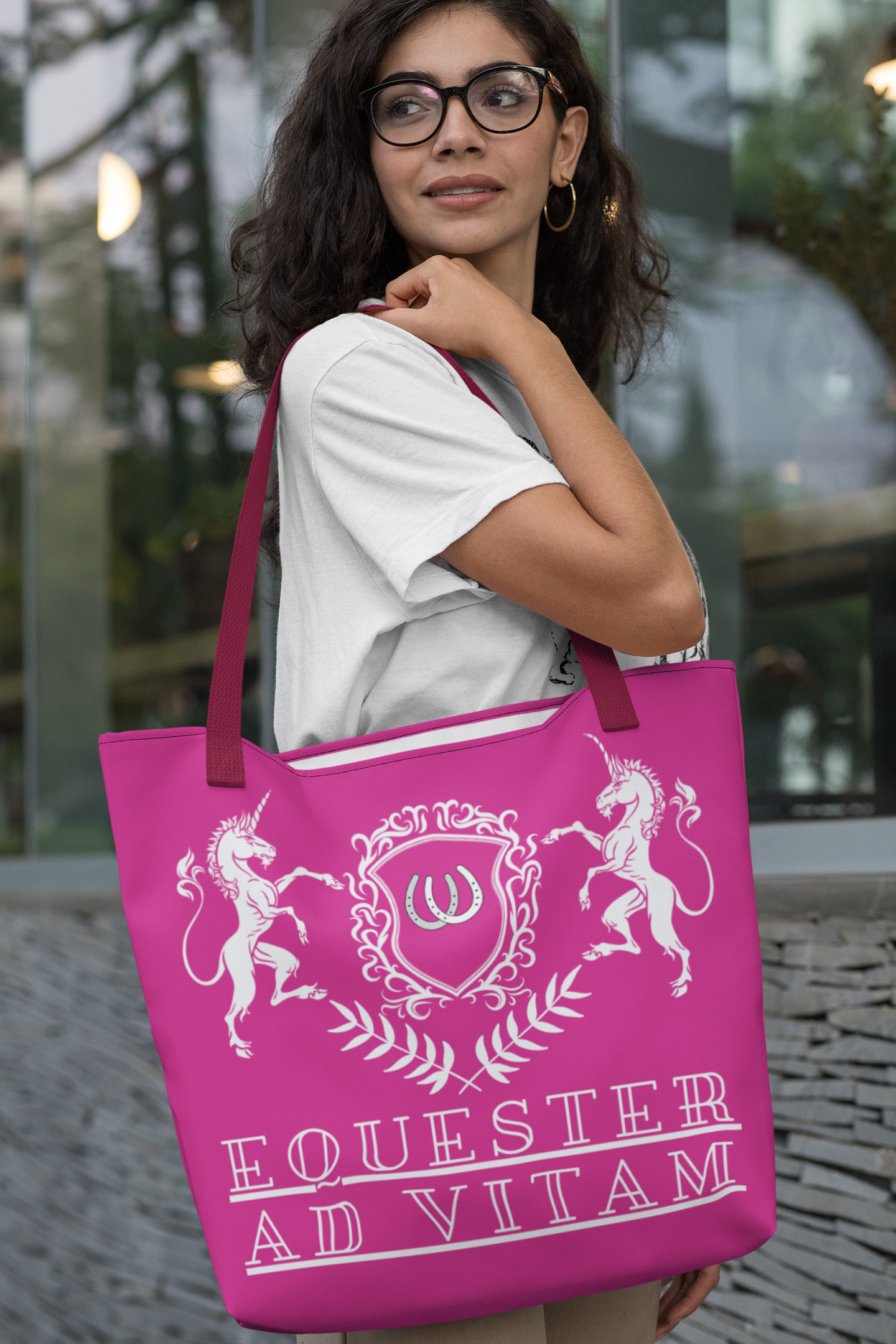 Woman holding a pink tote bag with a crest and text, standing outdoors.