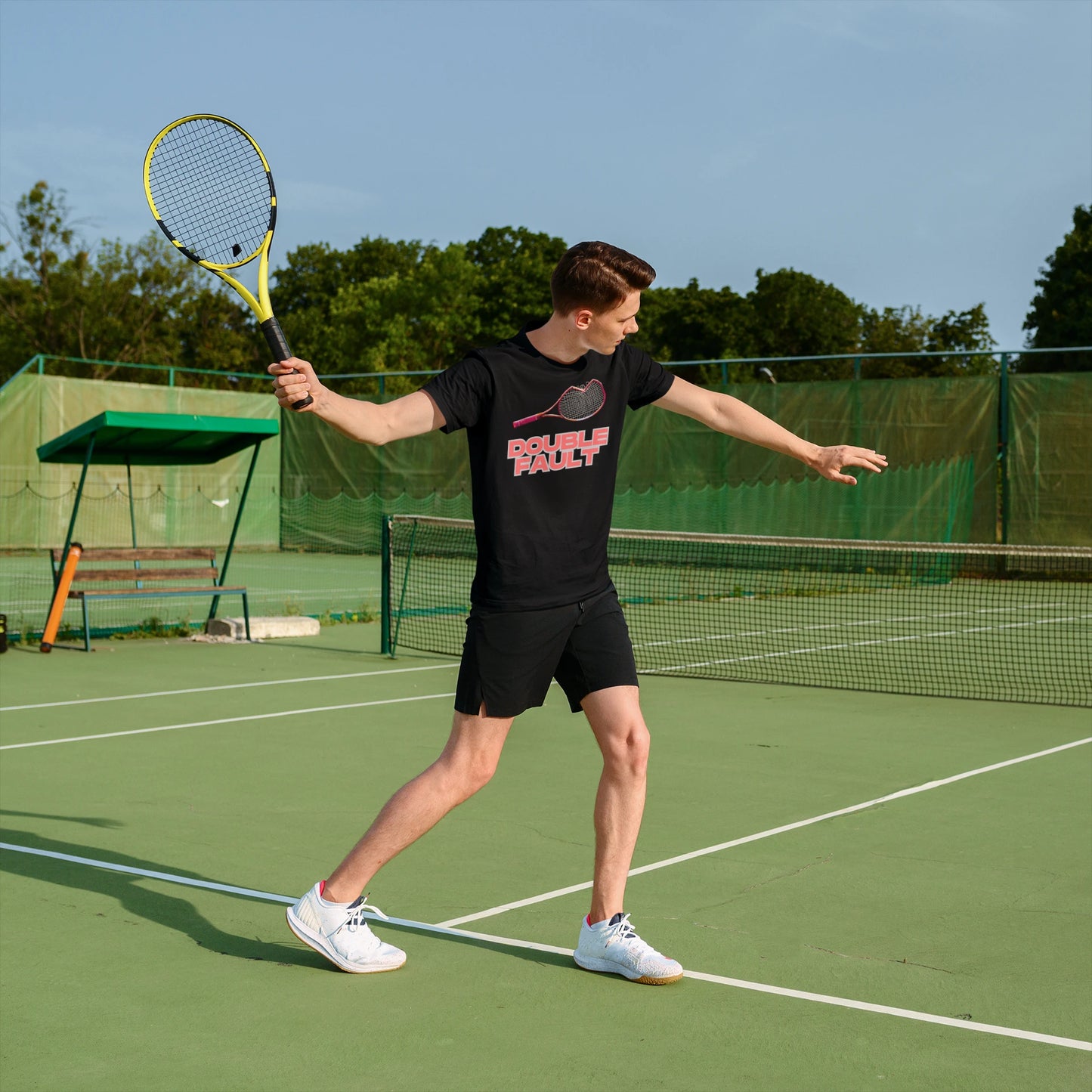 Double Fault Tee Person on a tennis court holding a racket with trees in the background