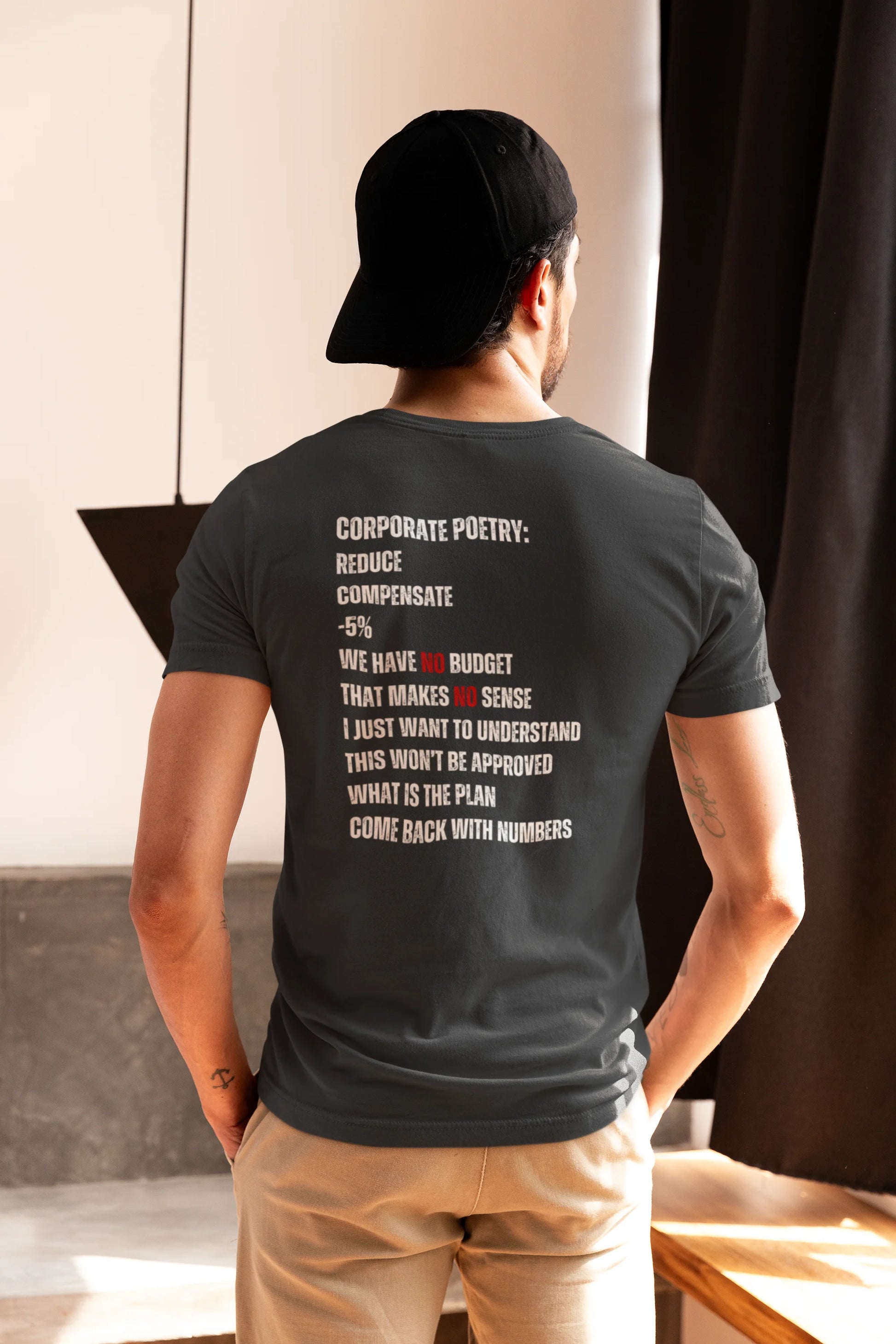 Finance Controller Shirt Person wearing a dark gray t-shirt with text on the back, standing indoors.