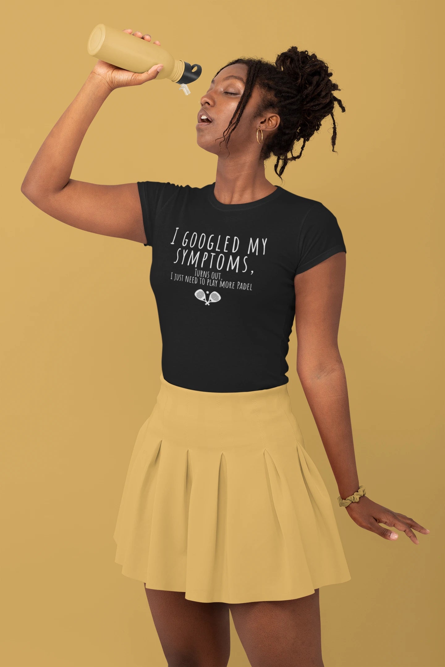 Woman wearing a black t-shirt with text and a yellow skirt, holding a bottle against a mustard yellow background