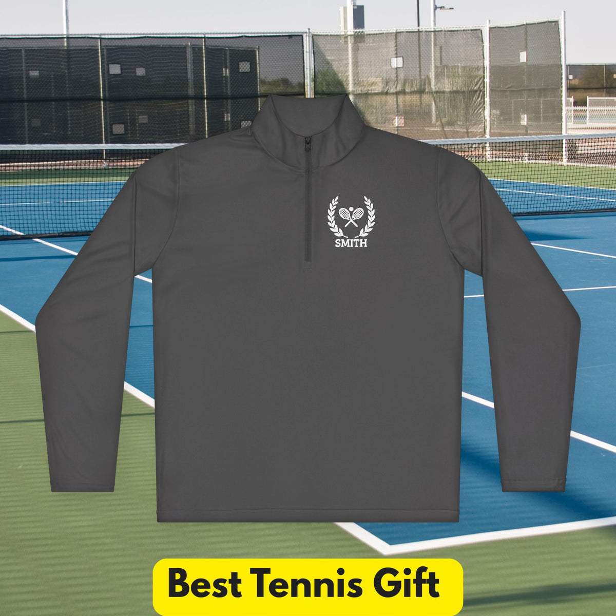 personalized tennis racket sweater A dark gray long-sleeve quarter-zip pullover with a white custom crest logo and the name 'SMITH' on the left chest, displayed against a tennis court background with a yellow 'Best Tennis Gift' banner at the bottom.